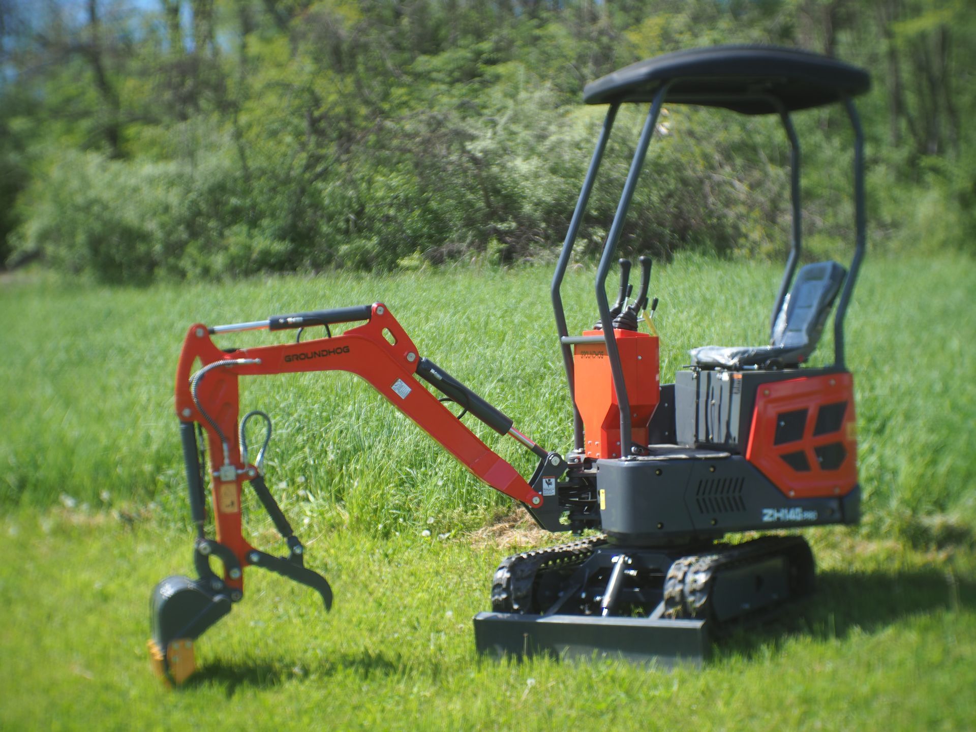 Orange and black mini excavator on grass in front of trees.