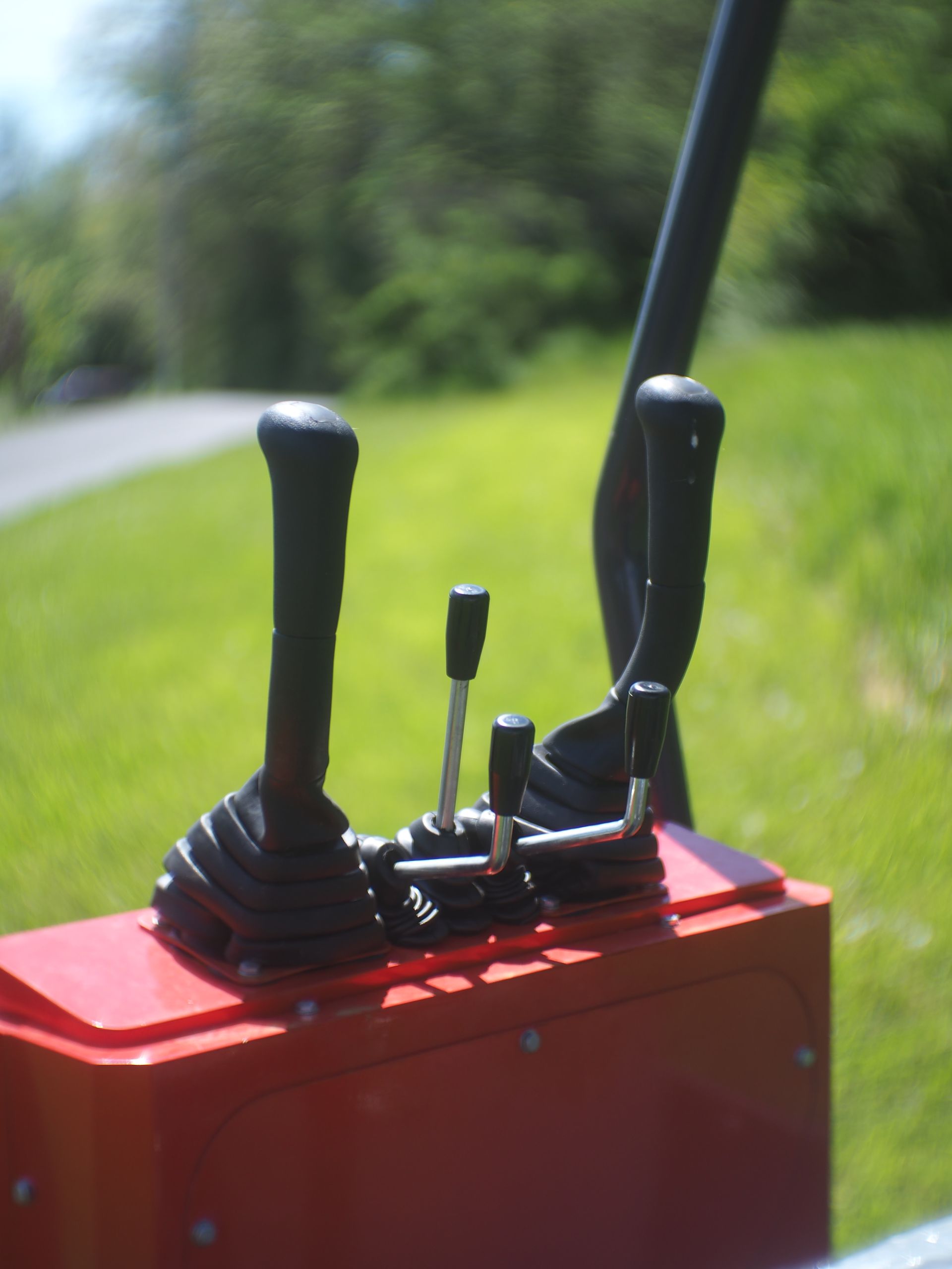 Red control panel with black levers against a blurred outdoor backdrop.