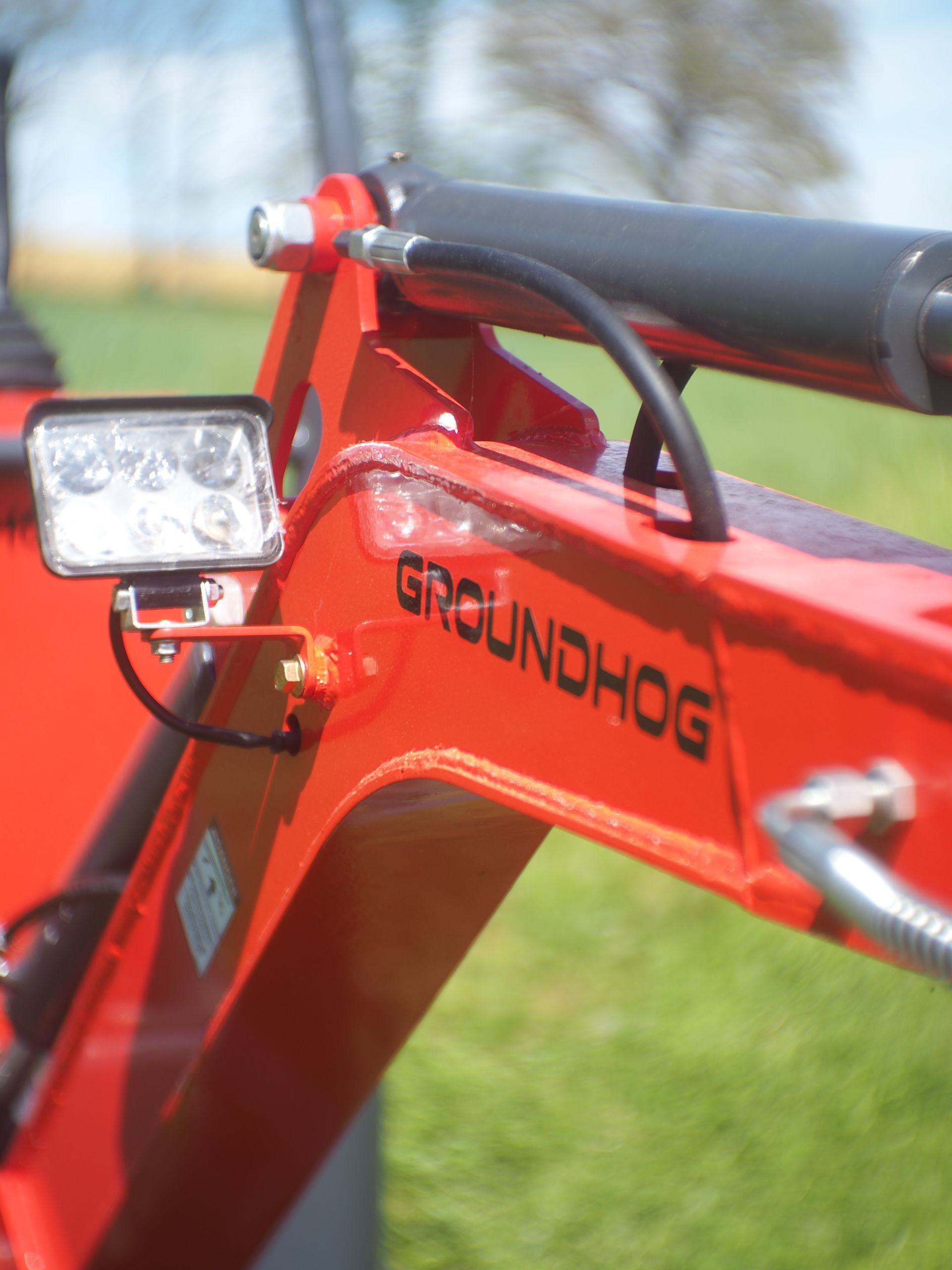 Close-up of a red Groundhog tractor arm with a bright work light attached.