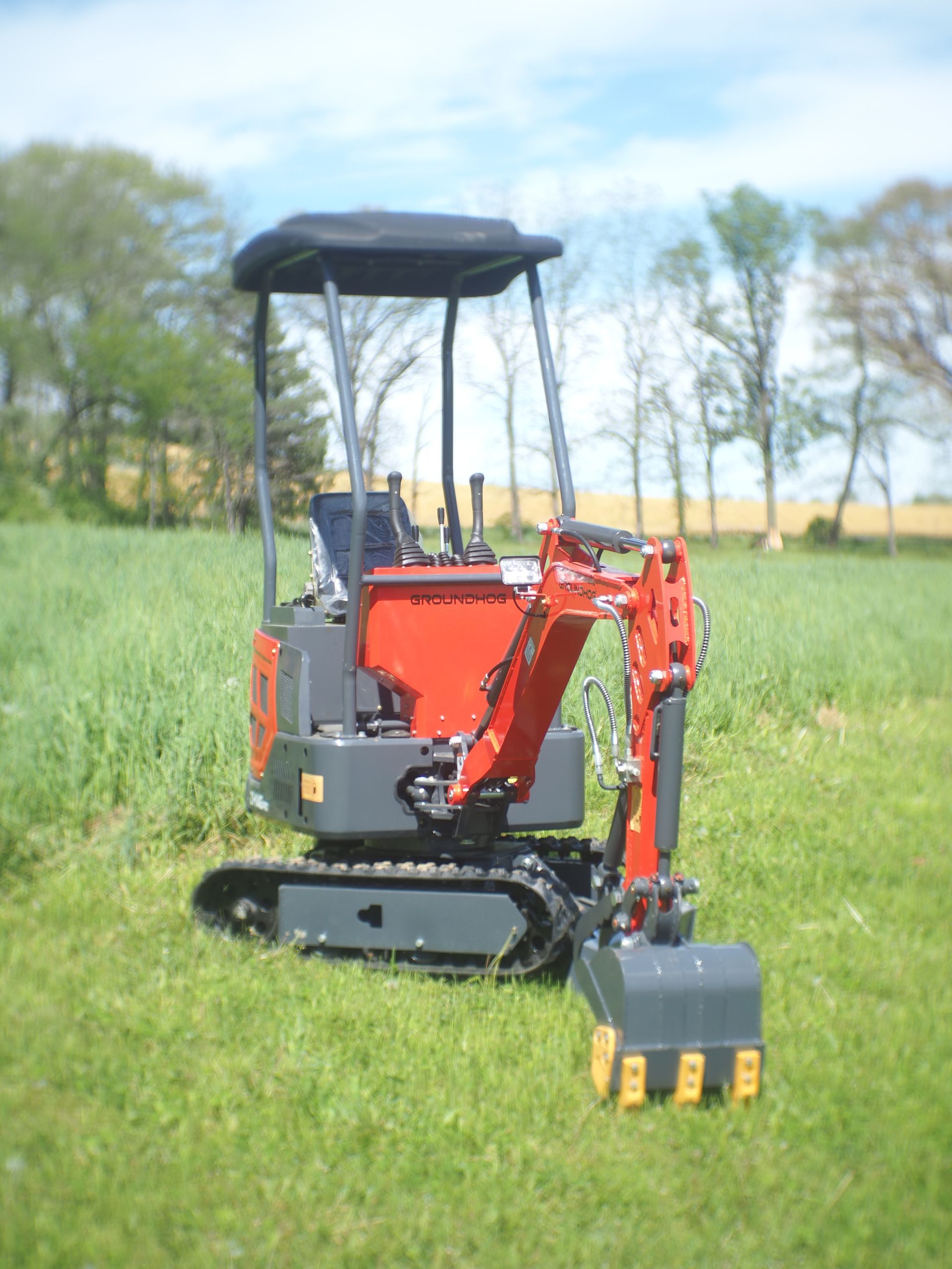 Red and gray mini excavator in a grassy field.