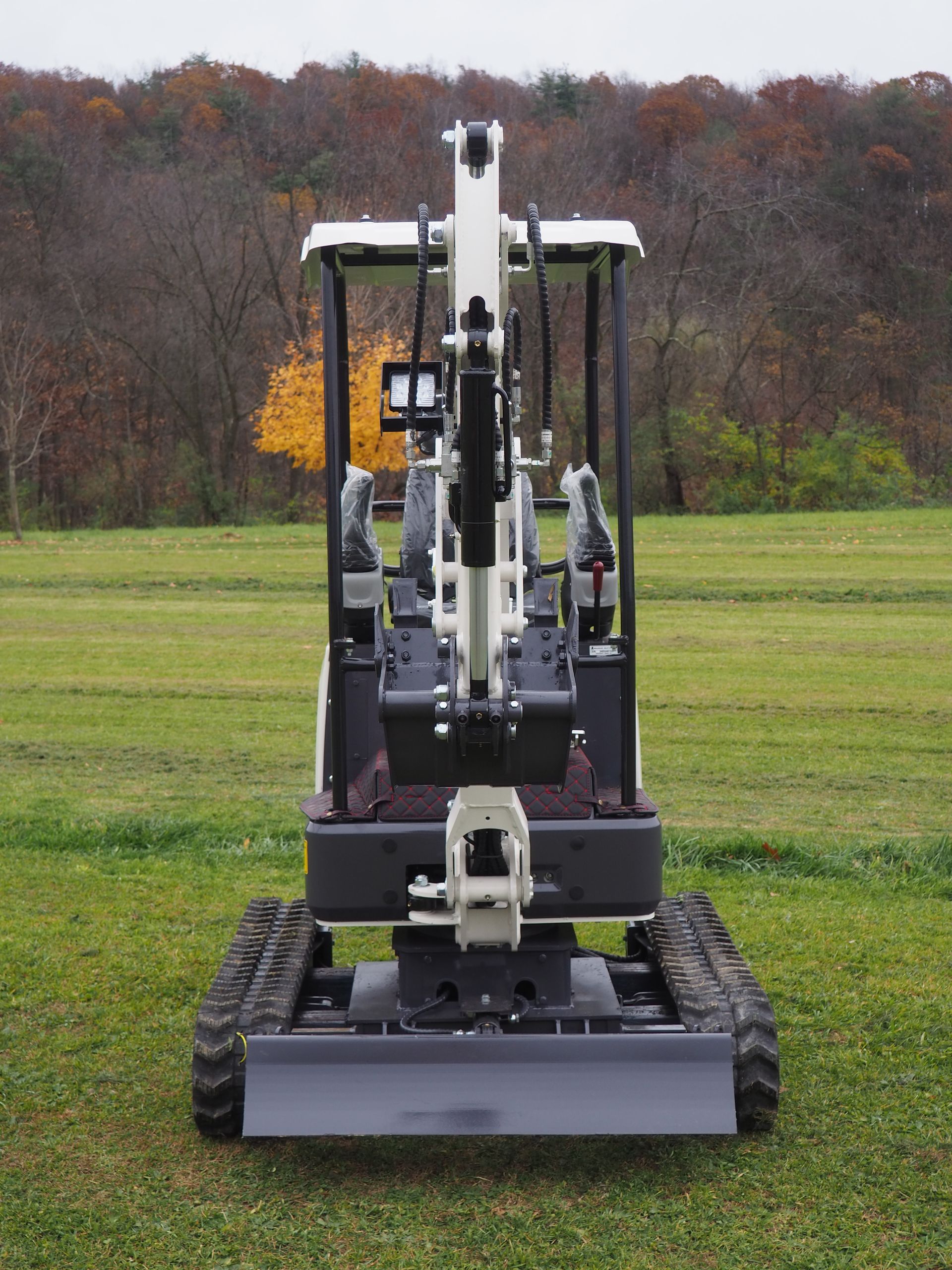 Mini excavator on tracks in a grassy field, facing forward. Gray and white machine.