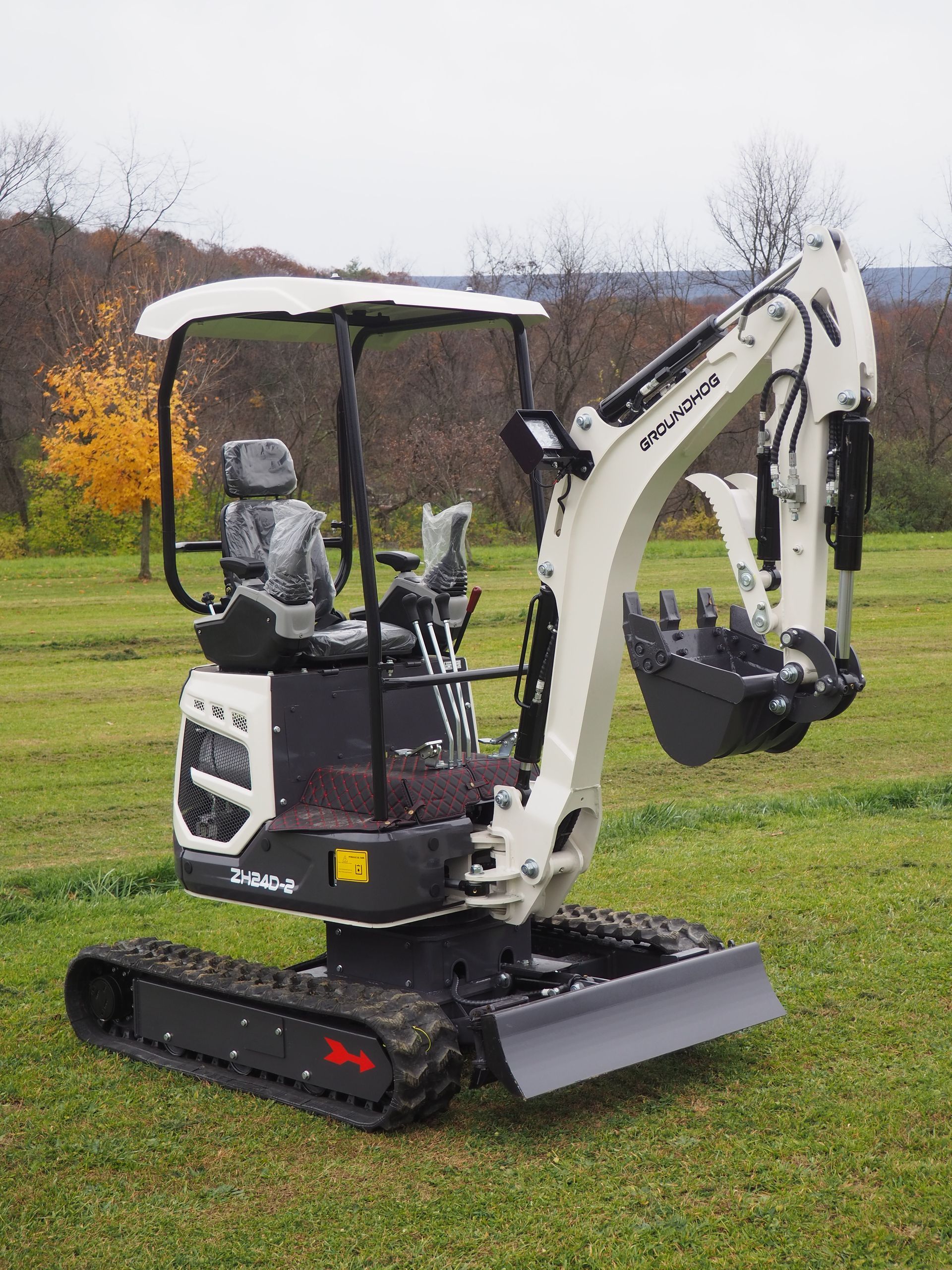 Mini excavator on grass. White and black, with raised digging arm.