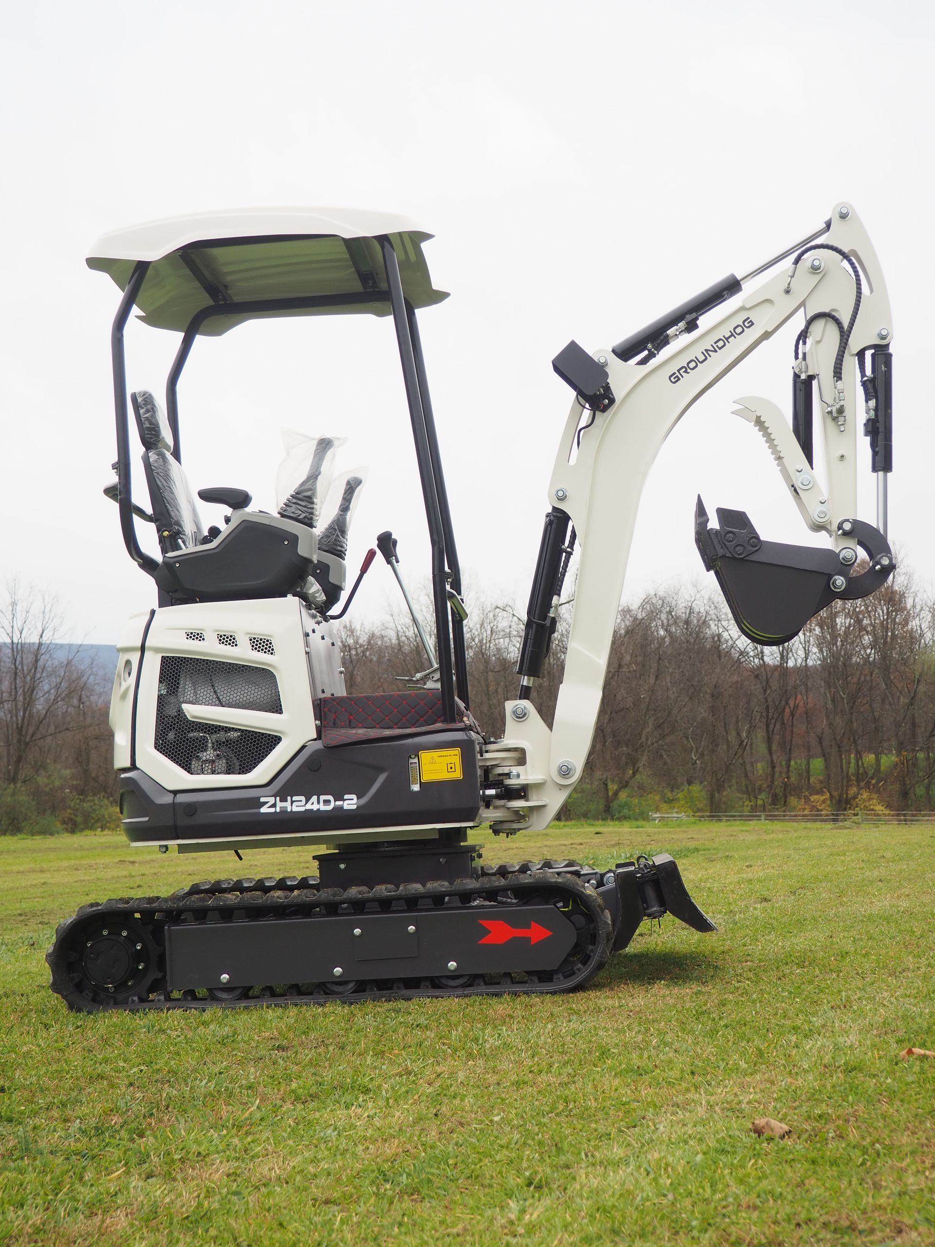 Small white and black excavator on tracks in a grassy field.