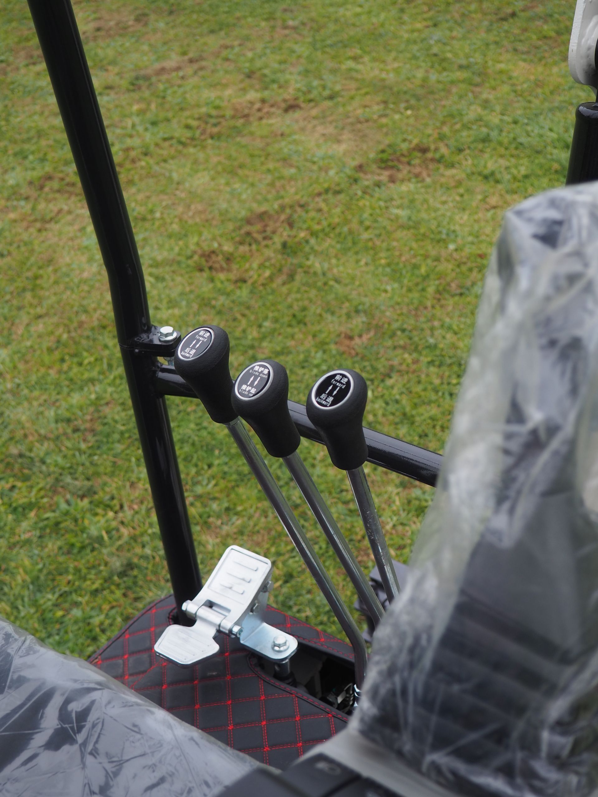 Levers and foot pedal in a tractor cockpit. Black controls on a black frame, plastic wrapped seat.