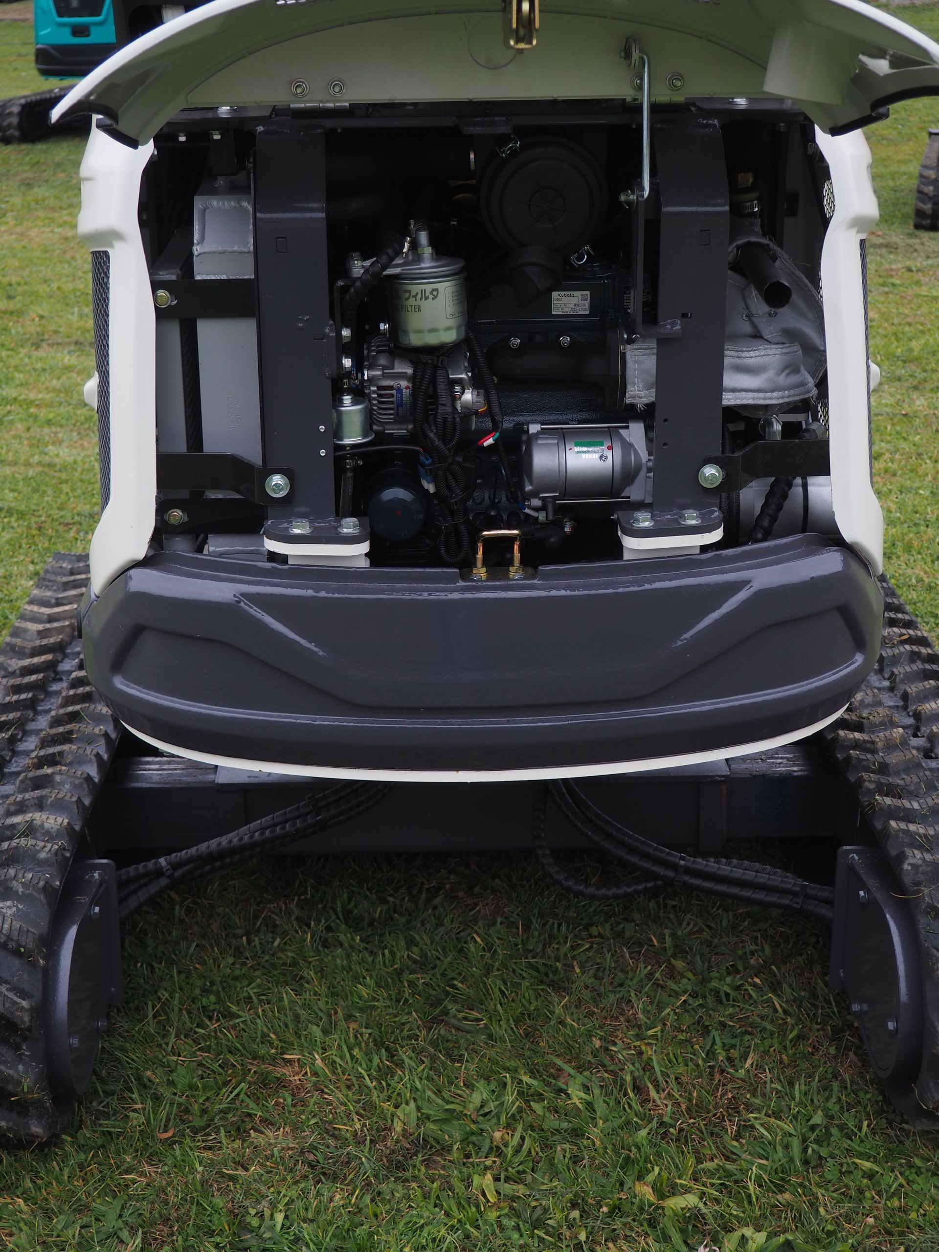 Front view of a small white excavator with a black engine. Black tracks are visible below.
