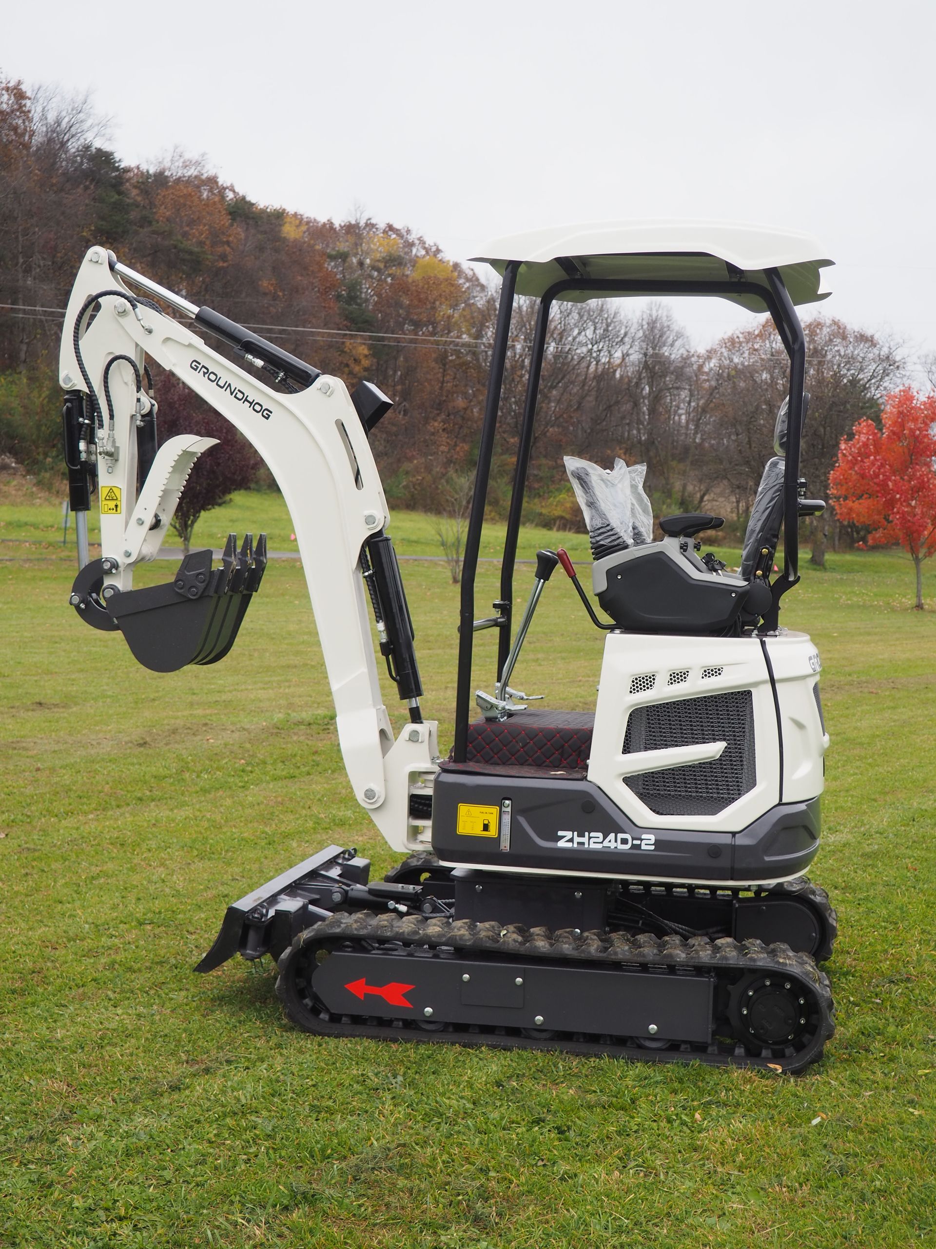 White and black mini excavator on green grass; trees in background.