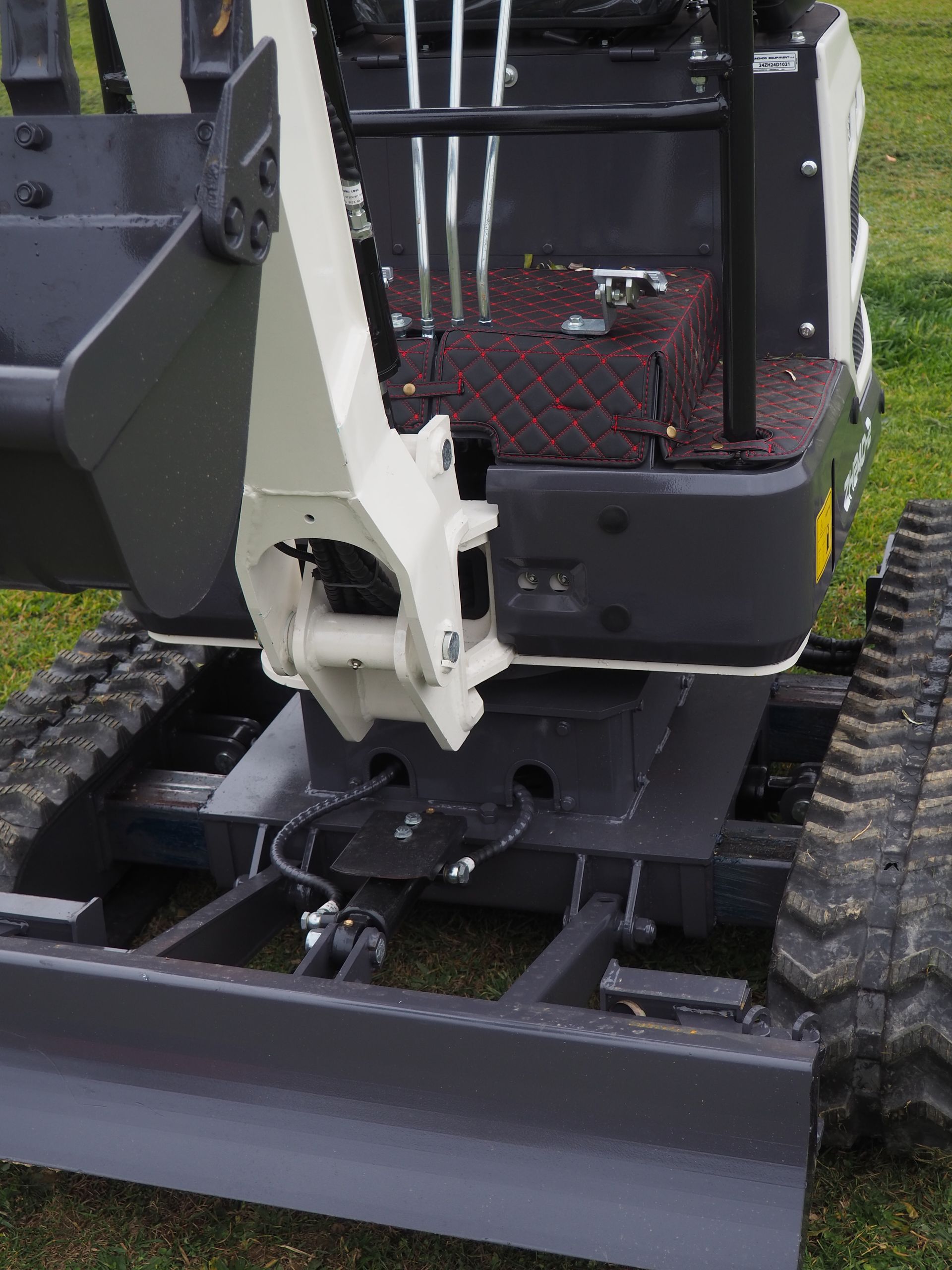 Mini excavator, gray and white, with tracks and a blade, outdoors.