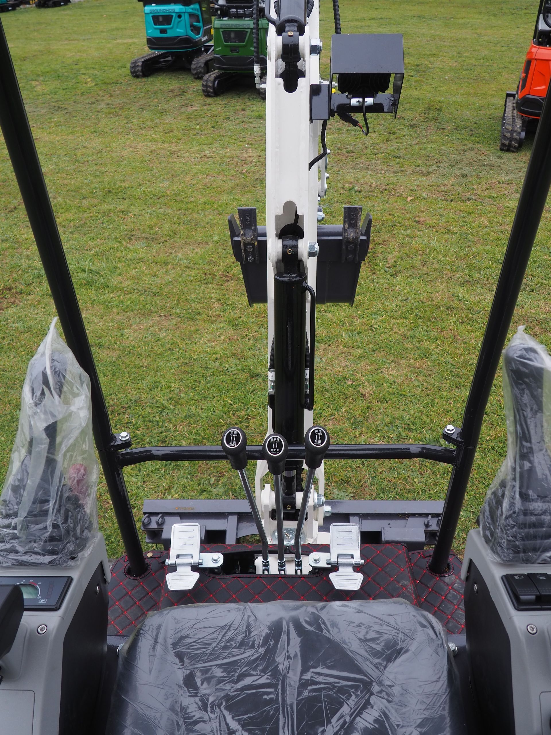 Interior view of a white mini excavator with control levers, a black seat, and green grass in the background.