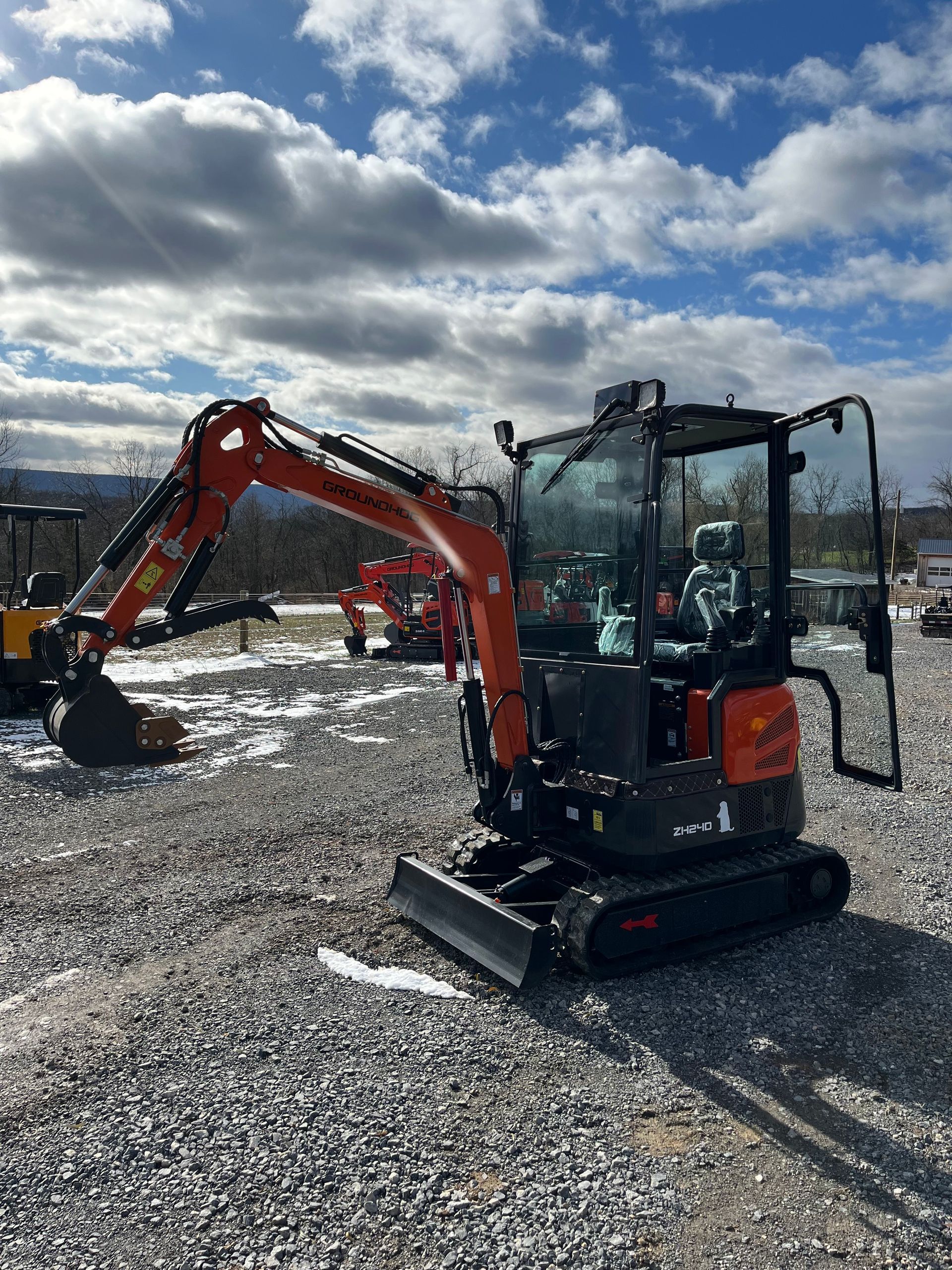 Orange Kubota mini excavator on gravel under a cloudy sky.