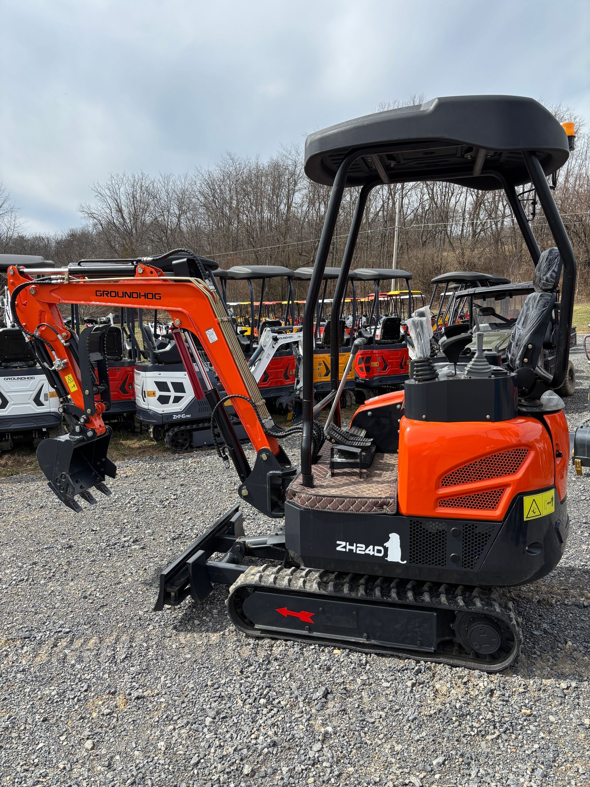 Orange and black mini excavator on gravel, with a black canopy, outdoors.