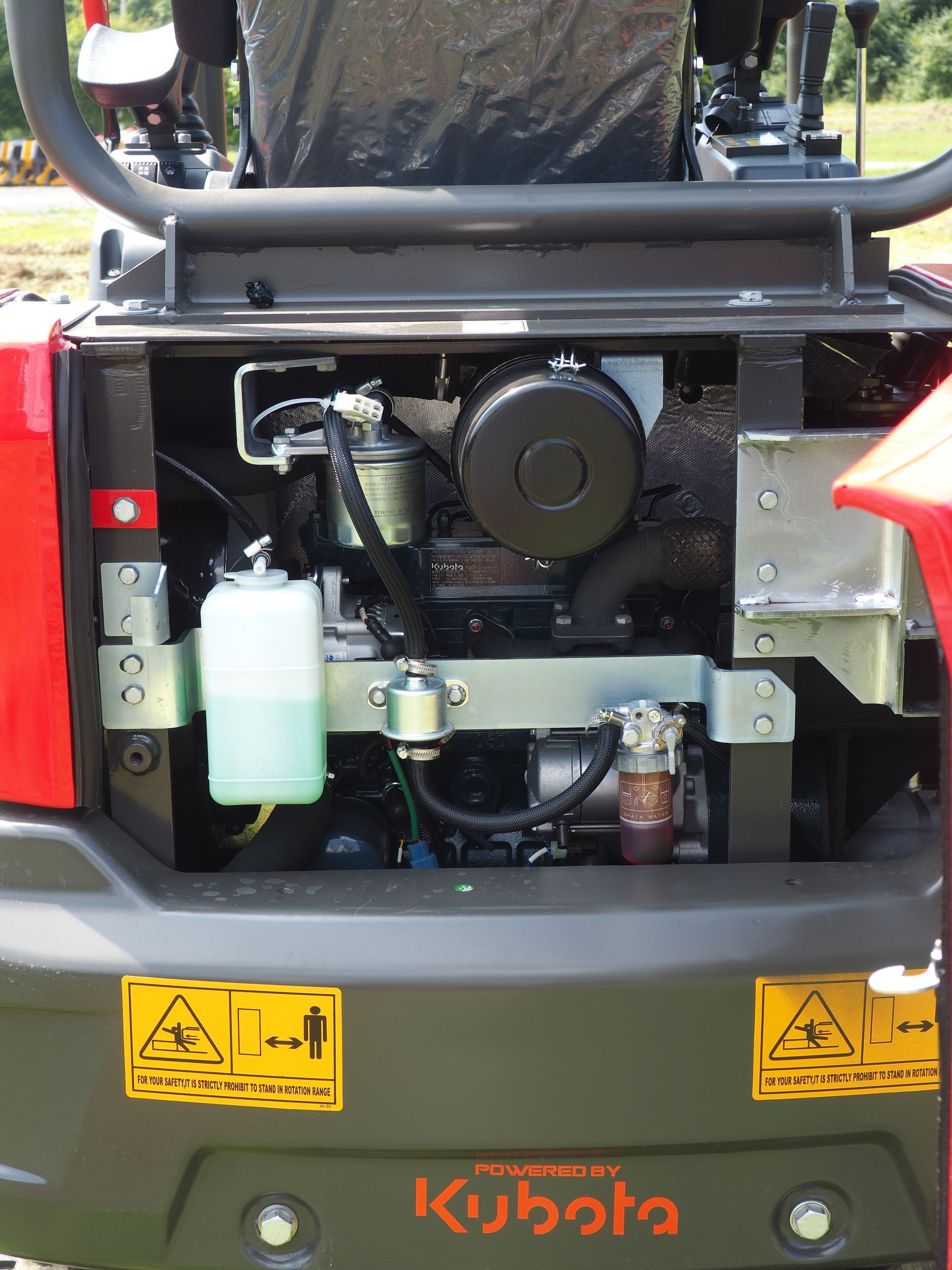 Close-up of the engine compartment of a red Kubota mini-excavator. Engine is black, coolant tank is white.