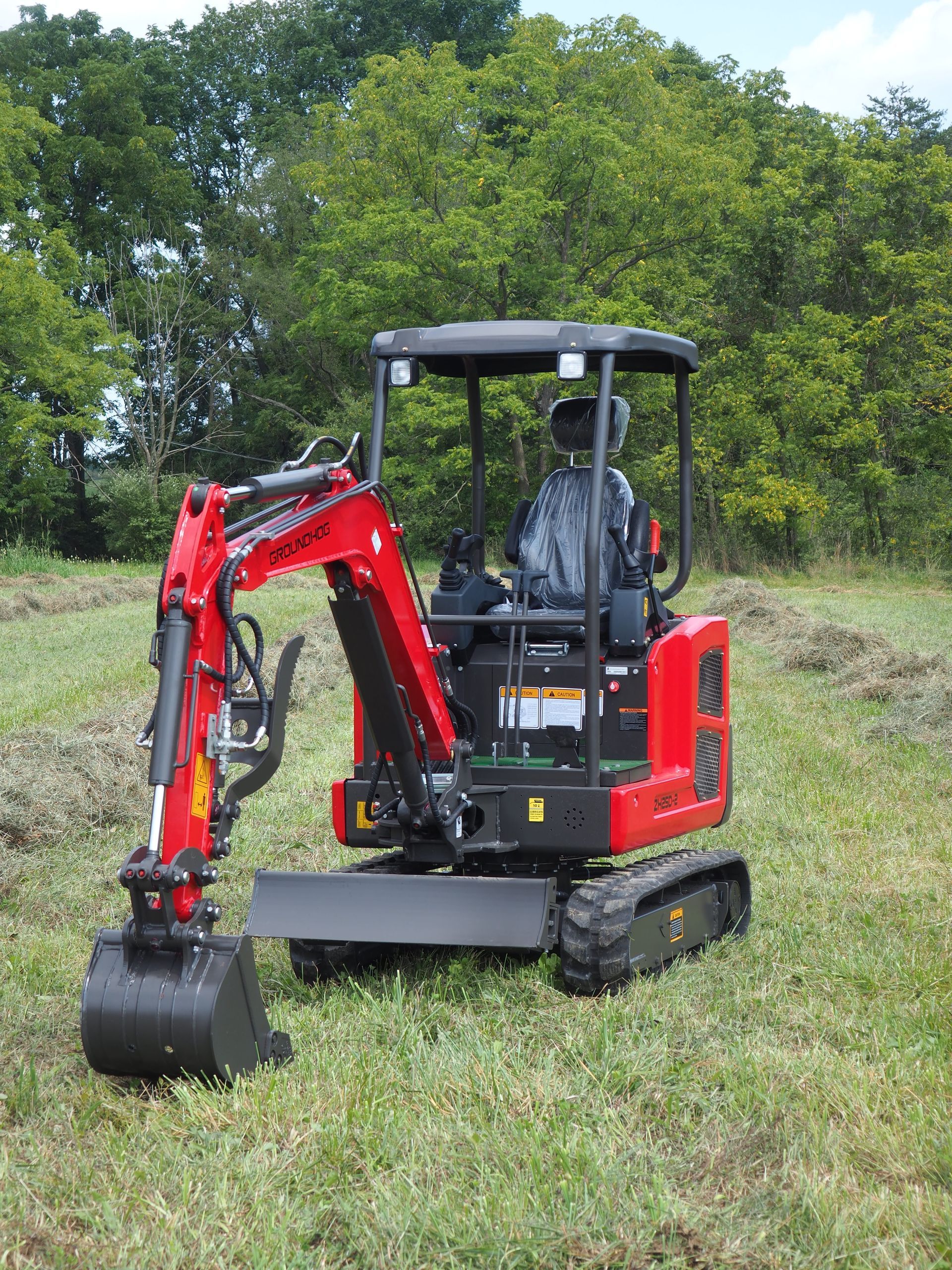 Red mini-excavator on grass, operating outdoors. A person is inside the cab.