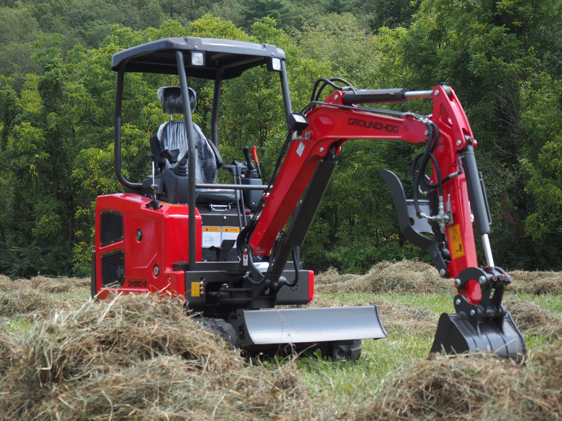 Red mini excavator on a field of hay, digging. A person is in the driver's seat.