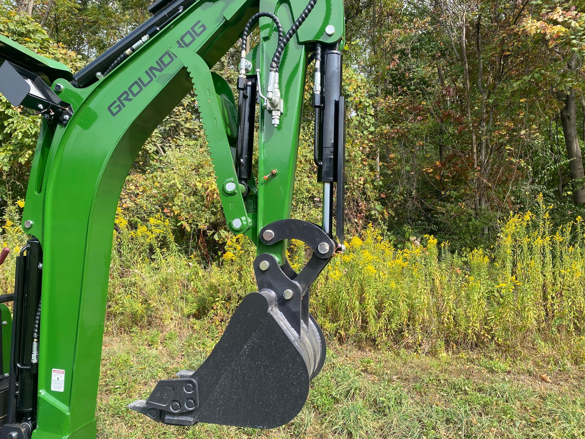 Green excavator arm with black bucket, outdoors near vegetation.