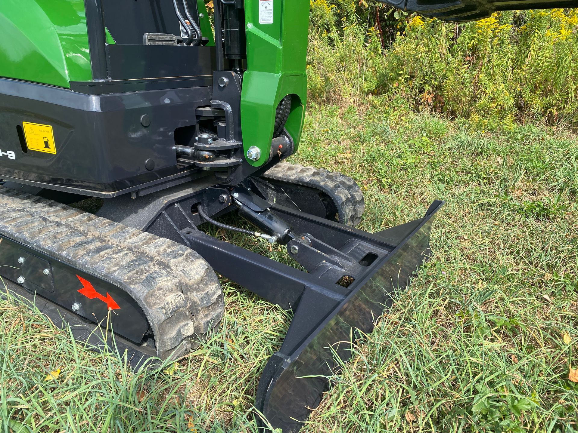 Green and black mini excavator with a blade in grassy field.