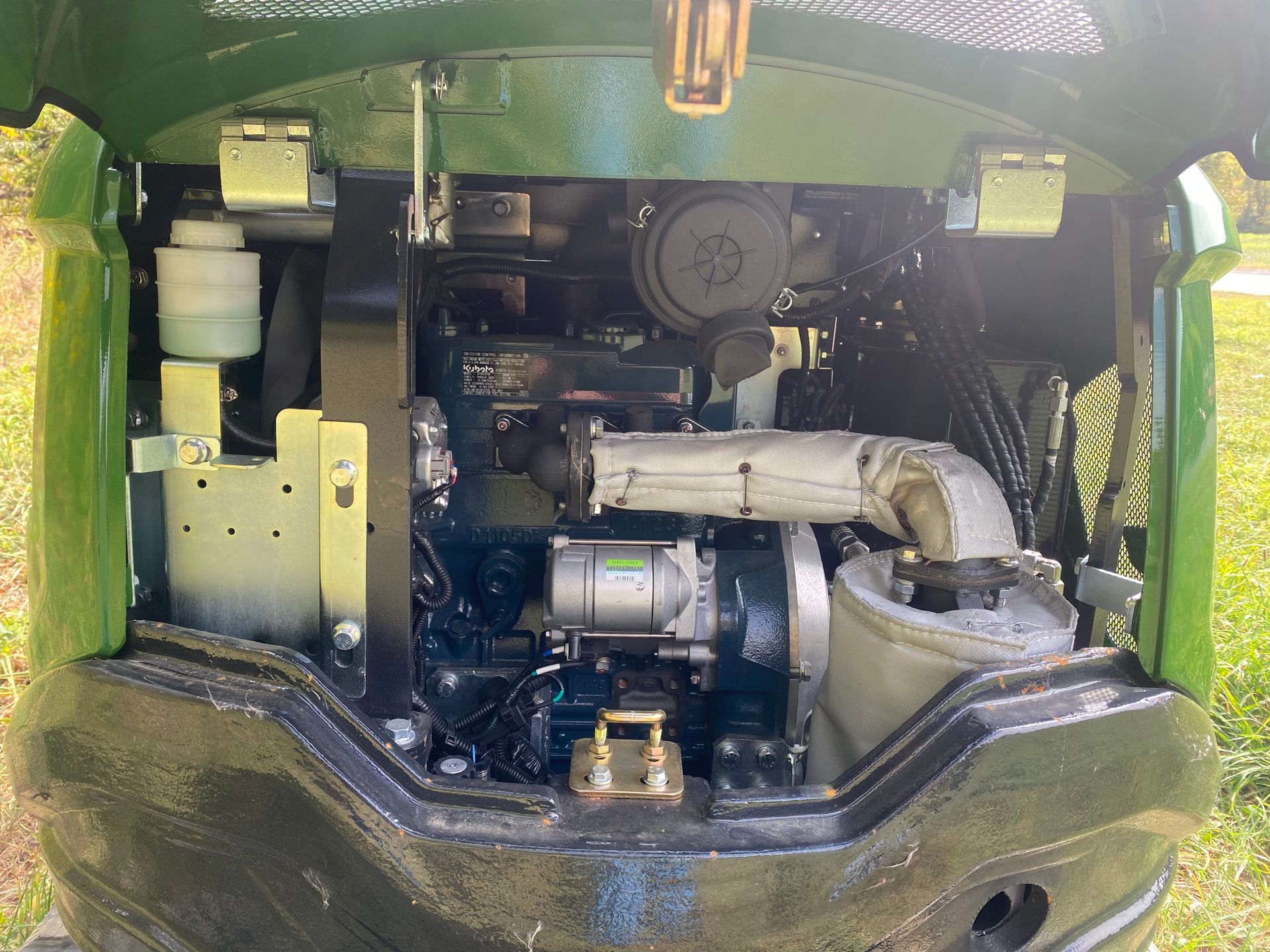 Green mini excavator engine compartment with various components visible.