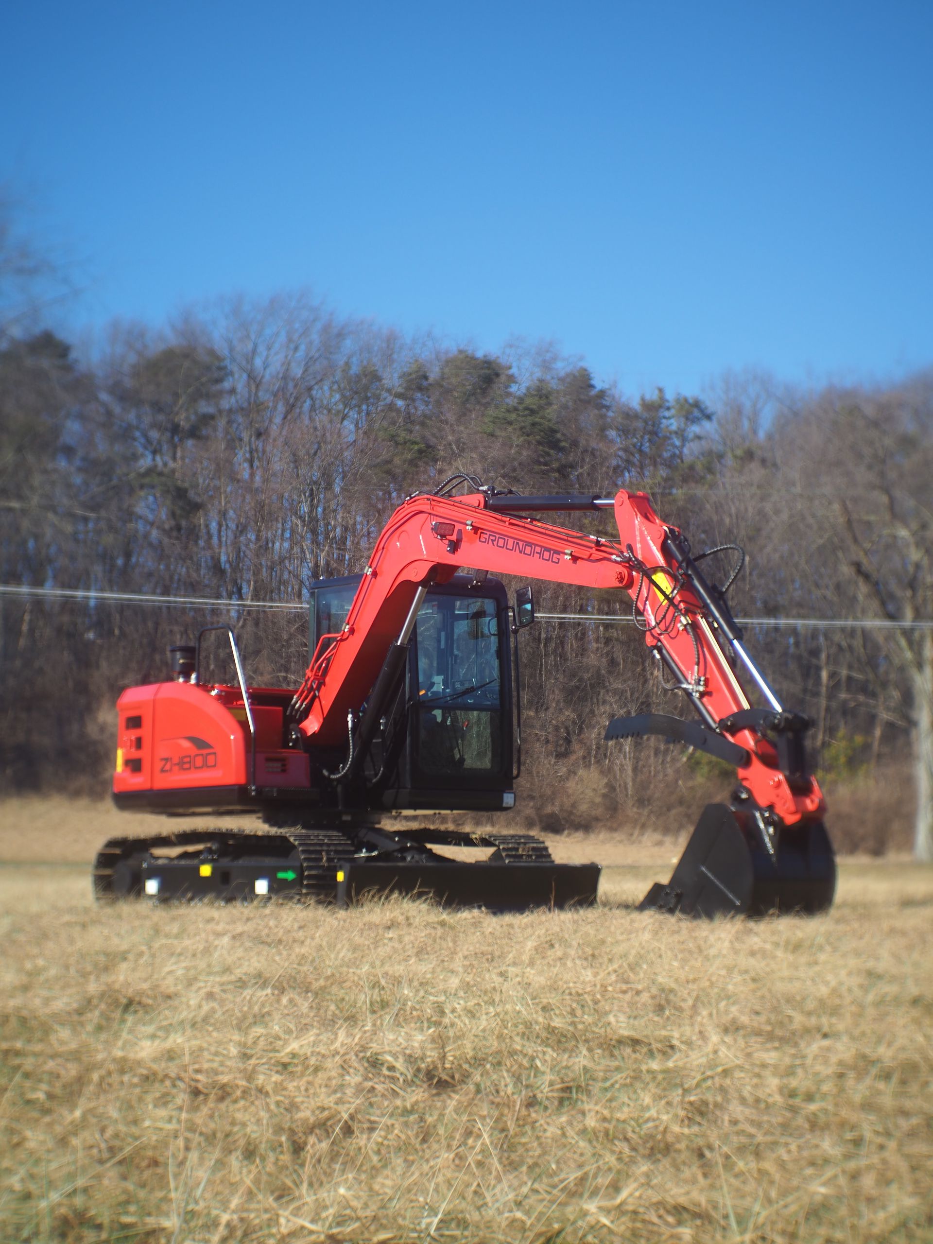 Red excavator on brown grass field under a clear blue sky.
