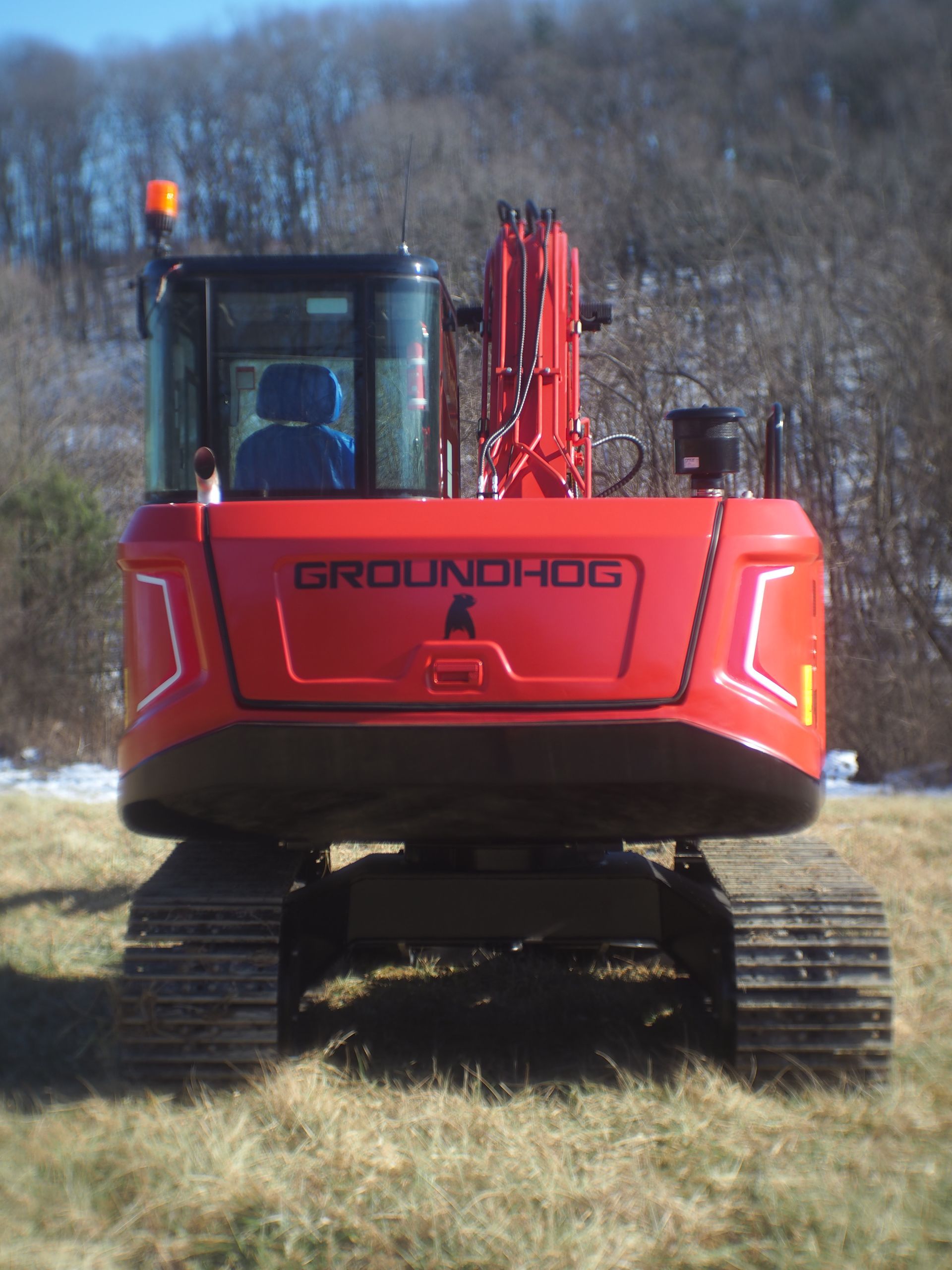 Red Groundhog excavator on tracks in a field, with a tree line in the background.