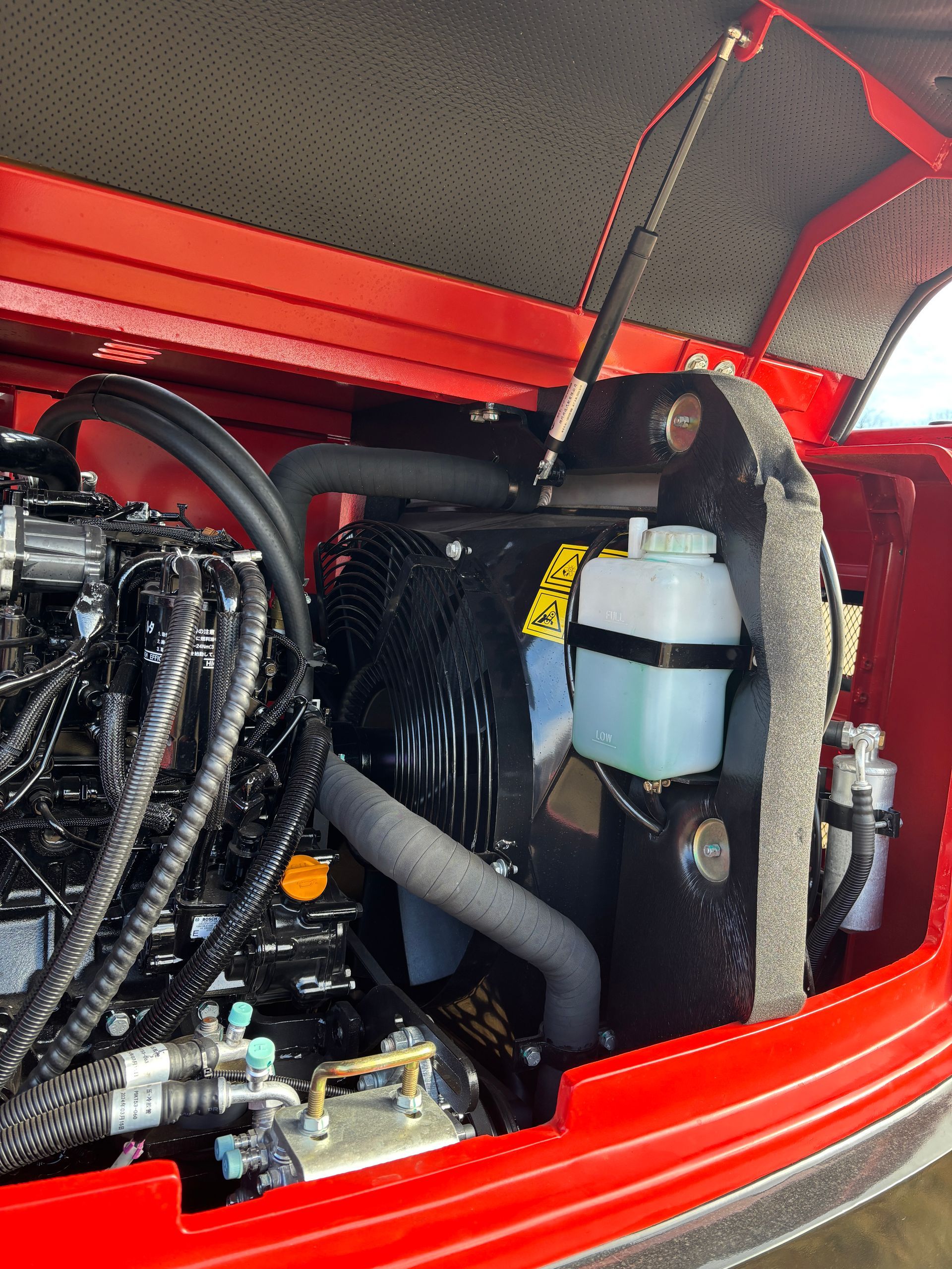 Black engine in red compartment, with a coolant reservoir and hoses.