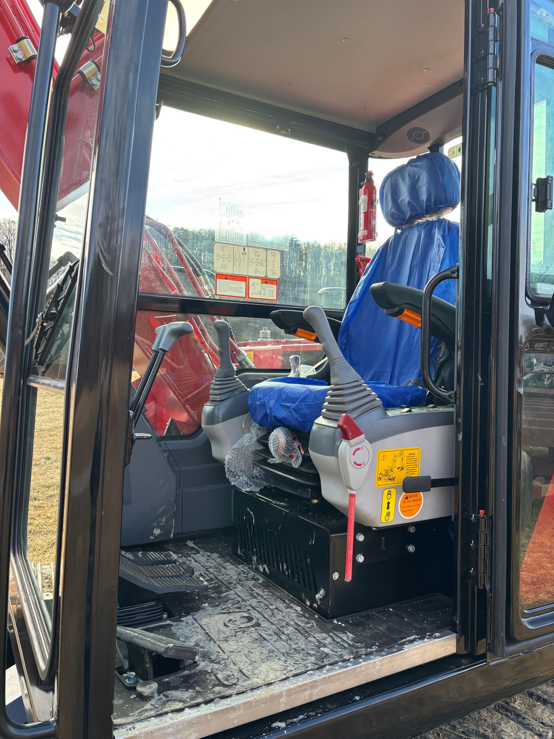 Interior of an excavator cab with a blue seat, red controls, and windows.