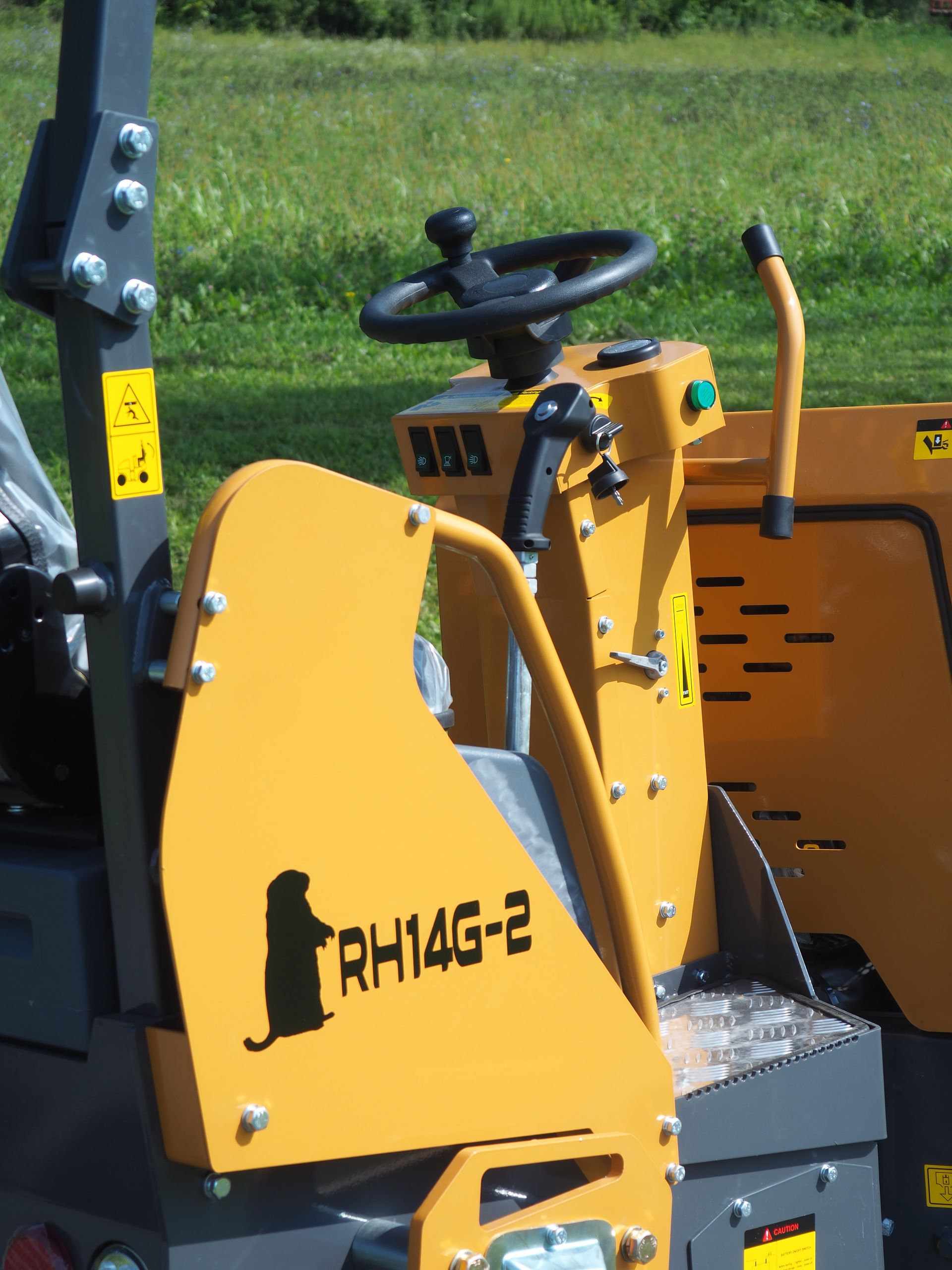 Yellow stump grinder control panel with steering wheel, lever, and RH14G-2 label, outdoors.
