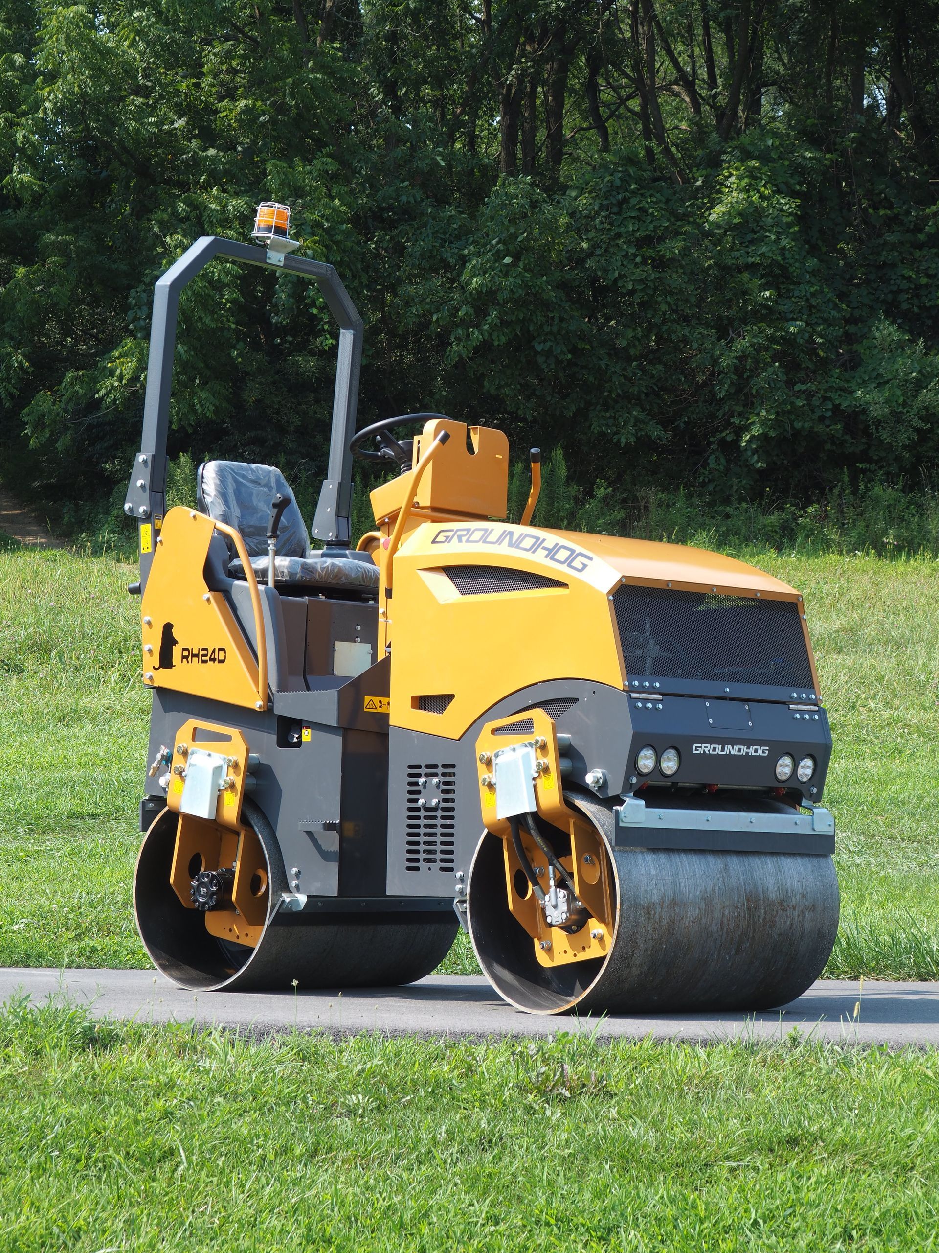 Yellow and black road roller compacting a paved surface on a grassy area.