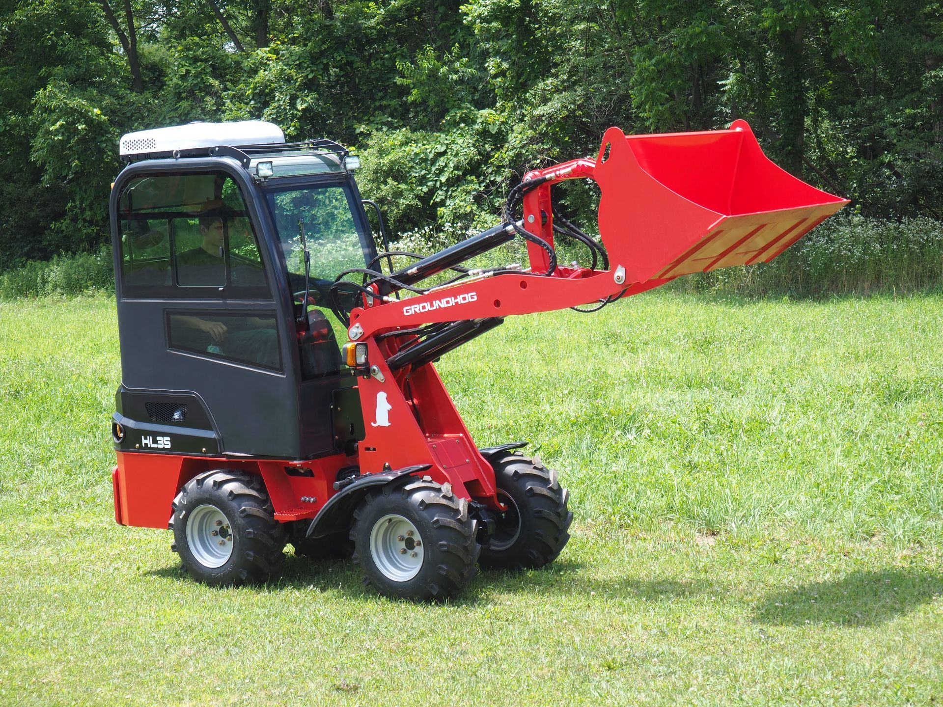 Red and black mini-skid steer loader with bucket on grass.