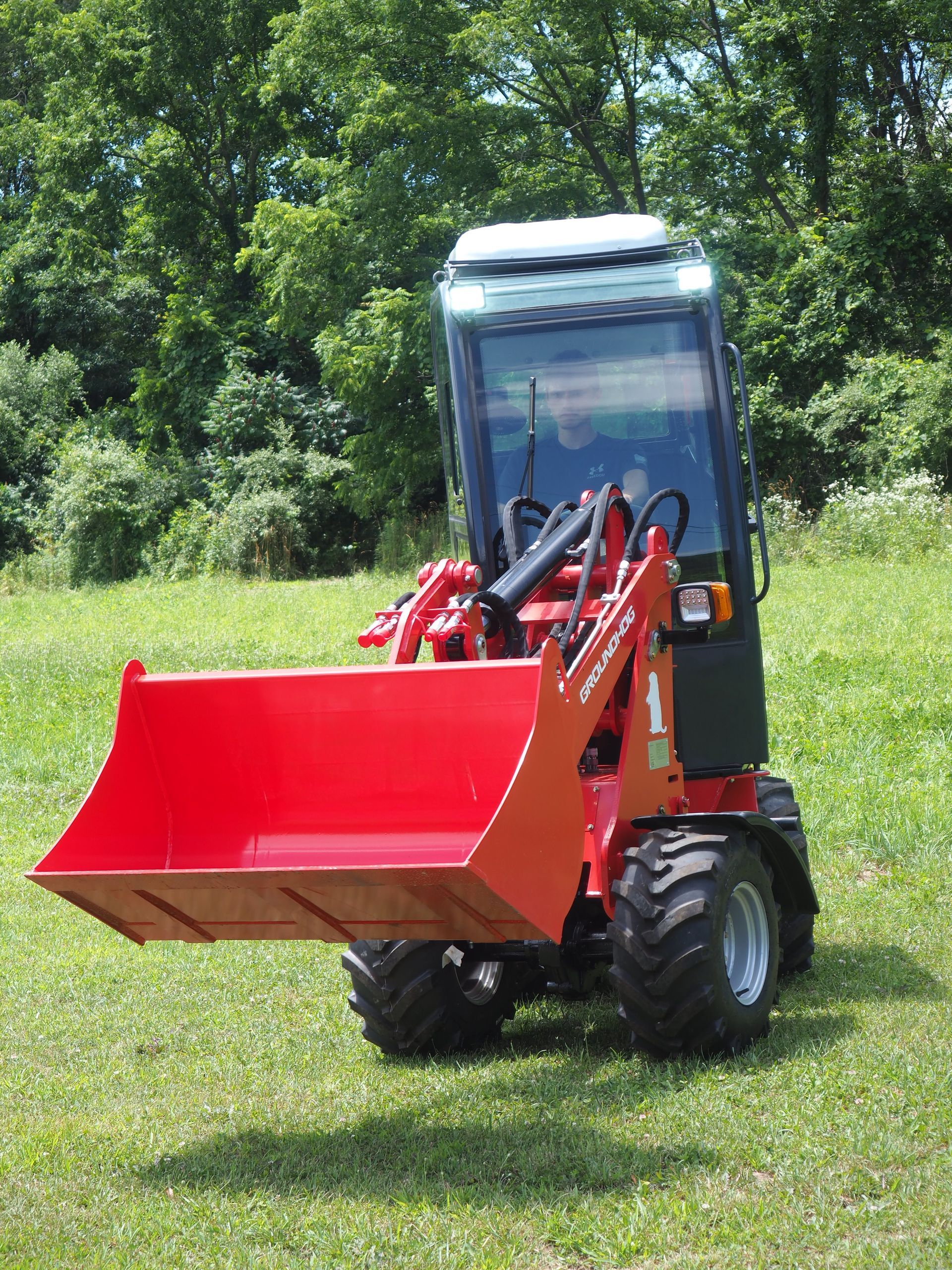 Red compact front loader on grass, with a cab.