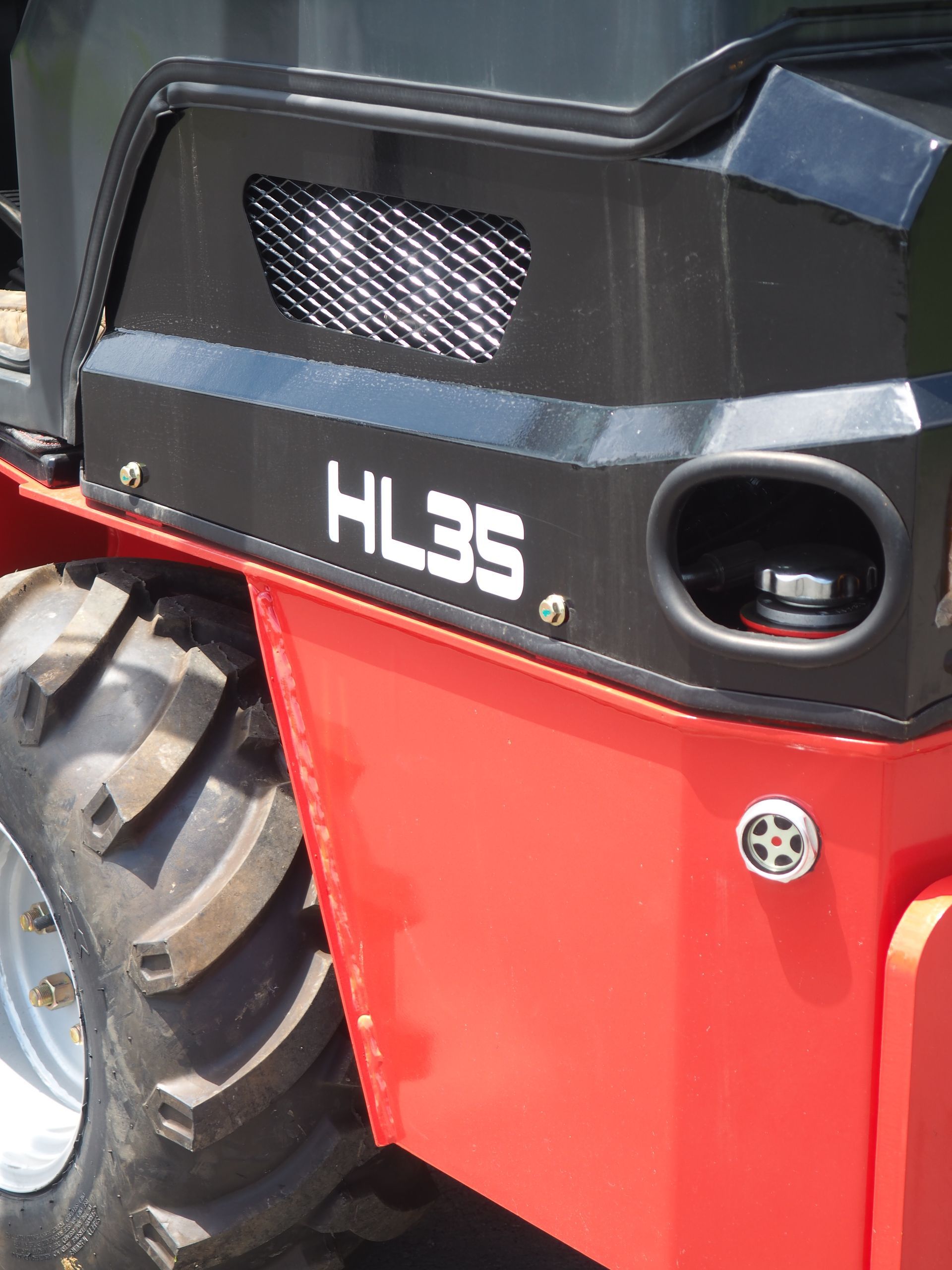 Red and black HL35 compact loader detail, showing tire, engine compartment, and fuel cap.