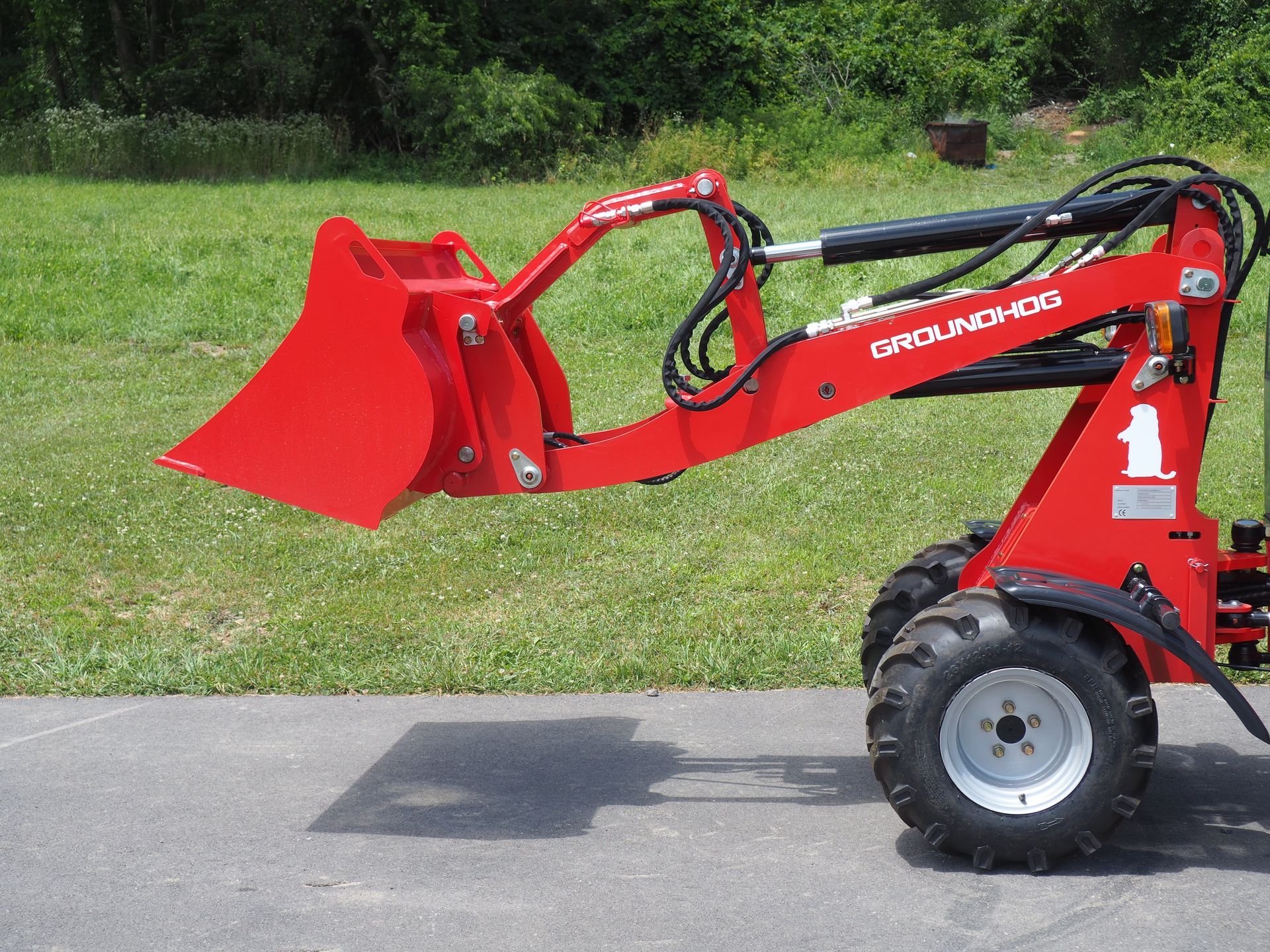 Red mini skid steer loader with bucket on asphalt.