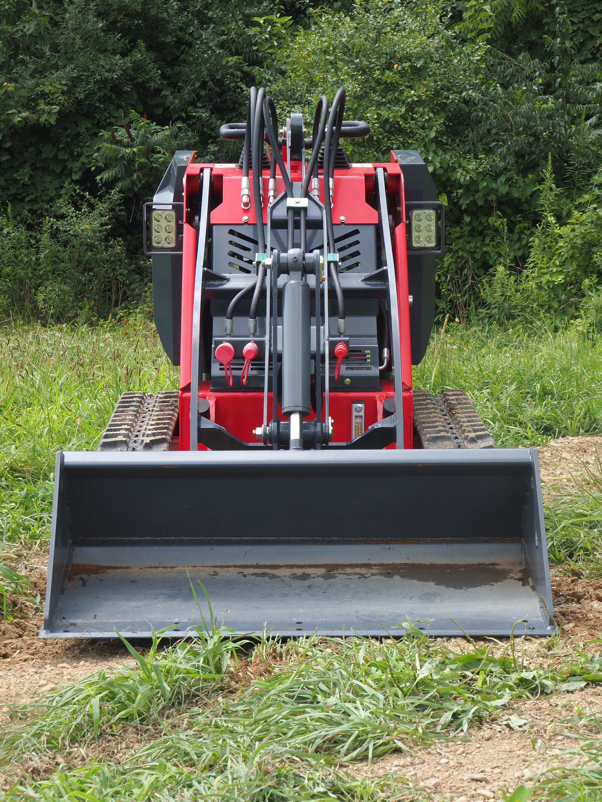 Red mini-skid steer loader with a bucket, on tracks, outdoors.