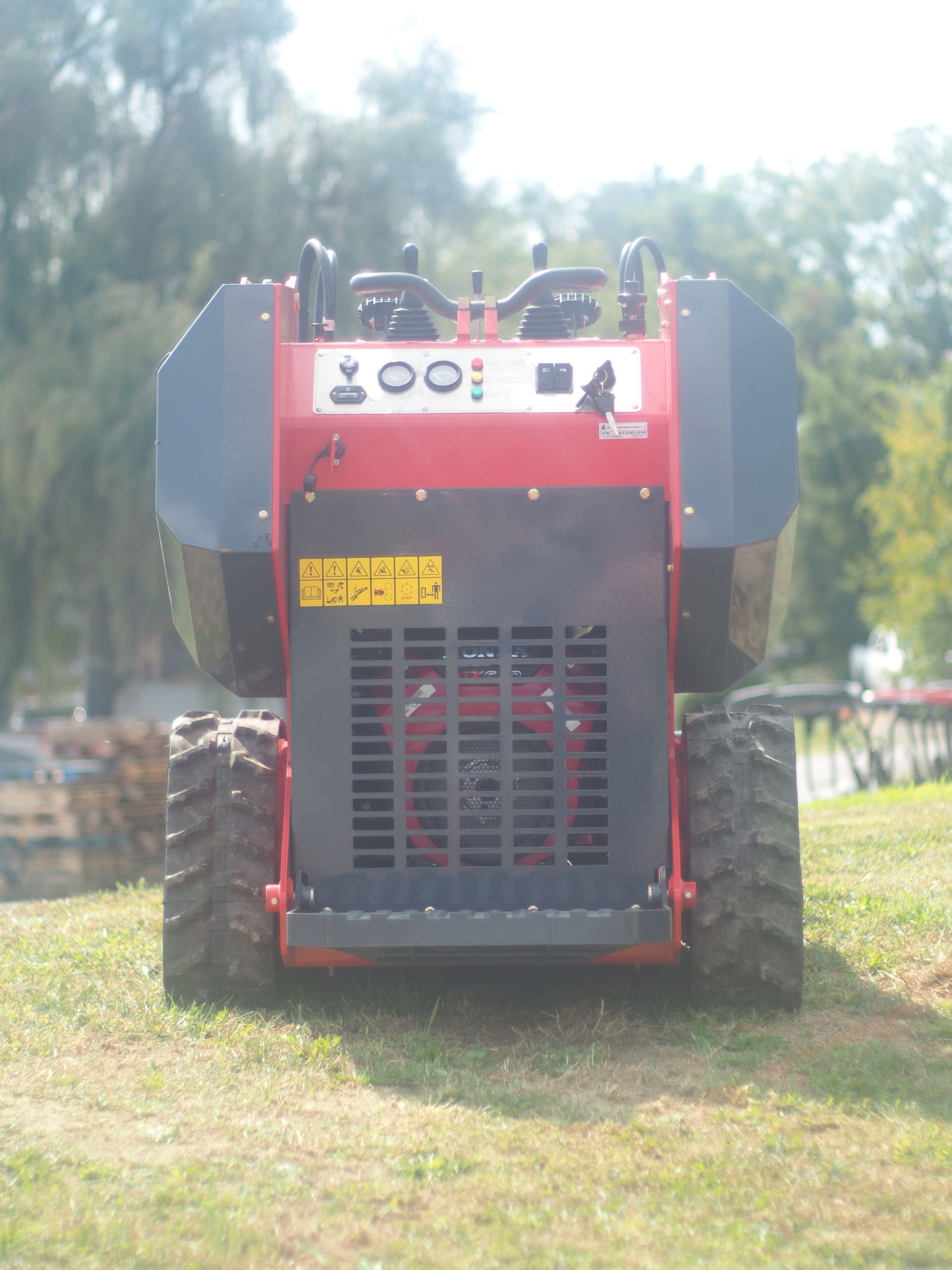 Red and gray mini skid steer on grass, viewed from the front.