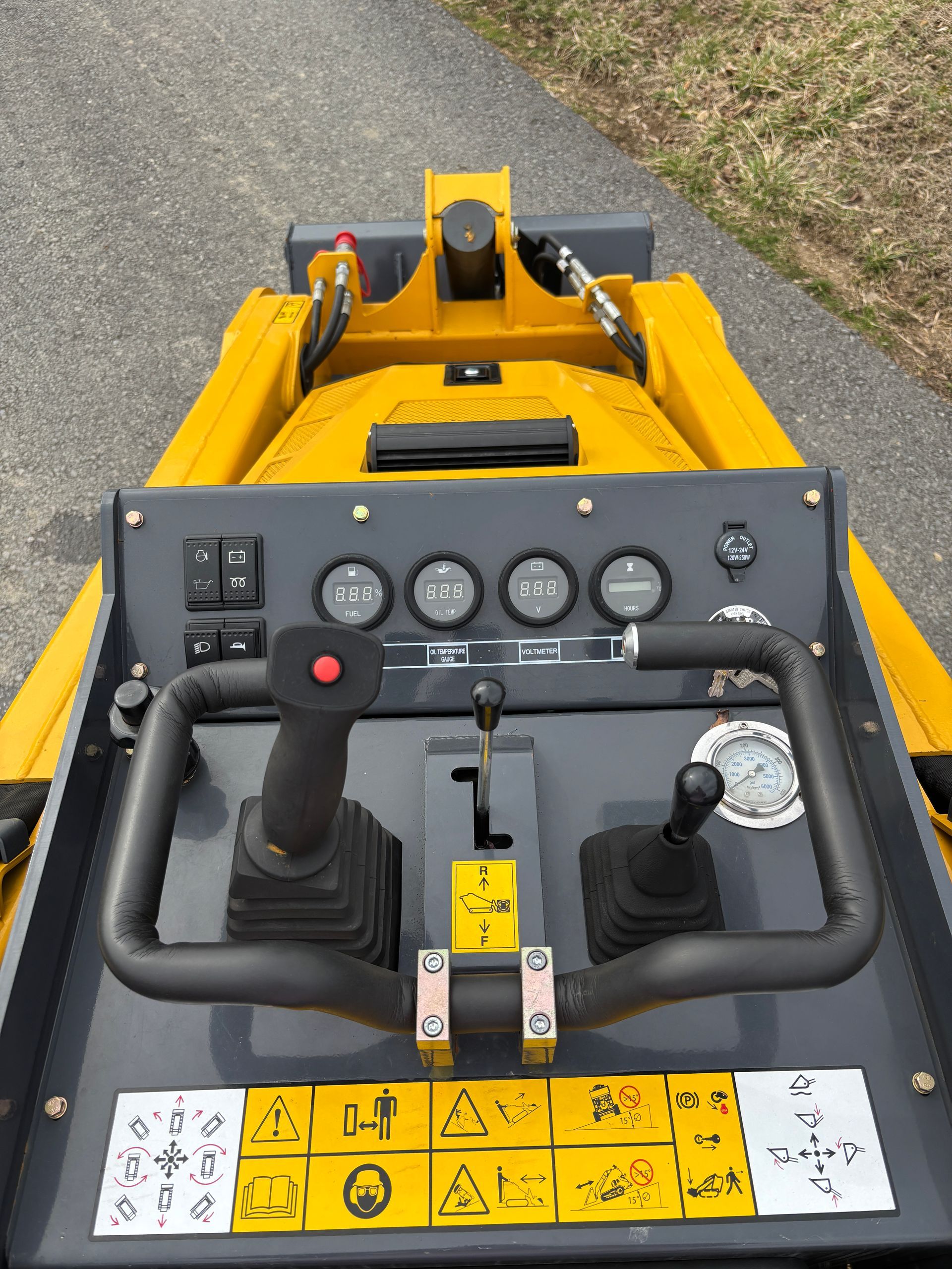 Yellow and gray construction equipment control panel with joysticks, gauges, and warning symbols.