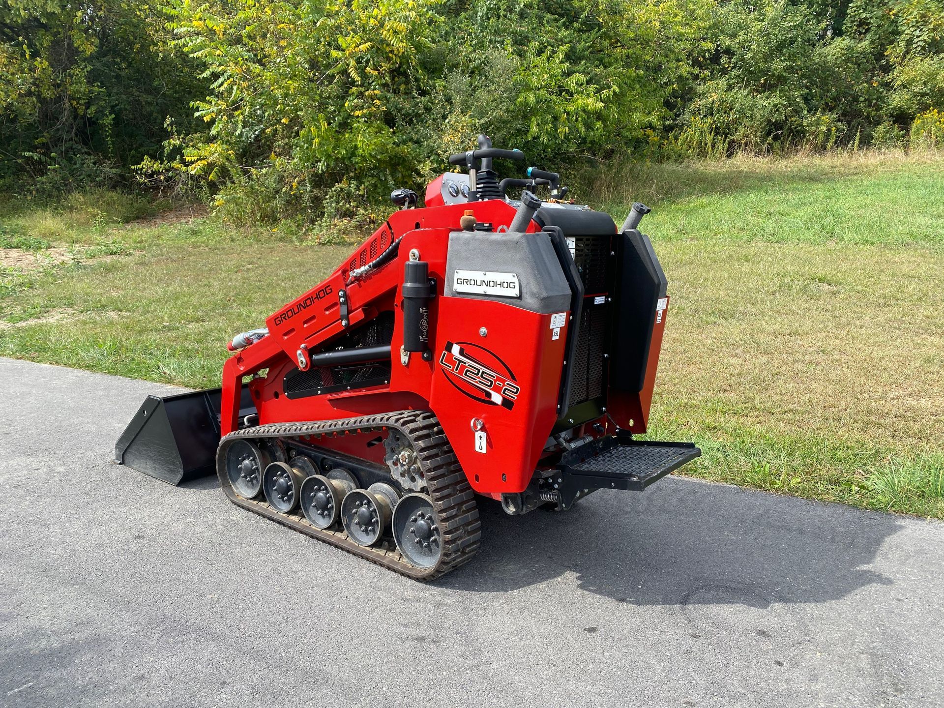 Red mini-skid steer loader with tracks on a paved path, outdoors.