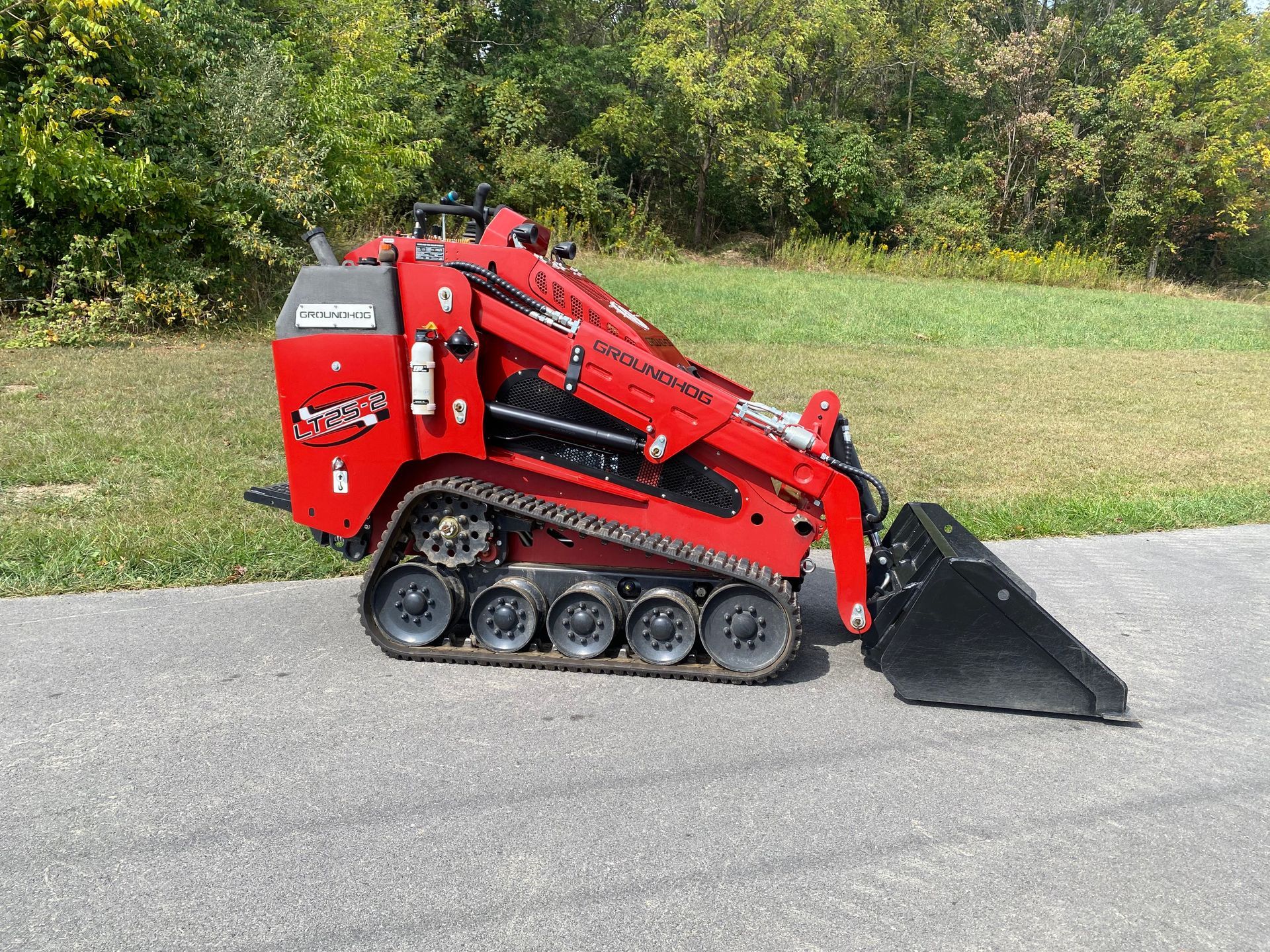 Red compact track loader with a bucket on a paved surface, outdoors.