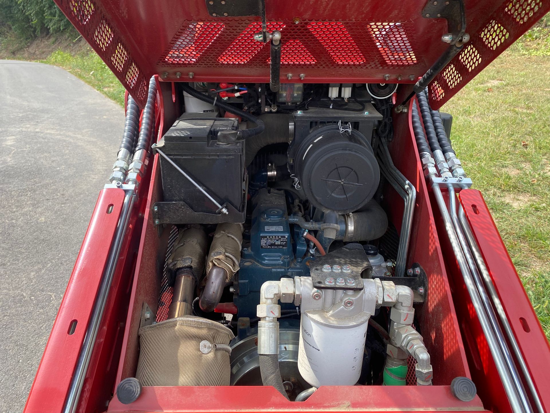 Open engine compartment of a red skid steer, showing a Kubota diesel engine and various components.
