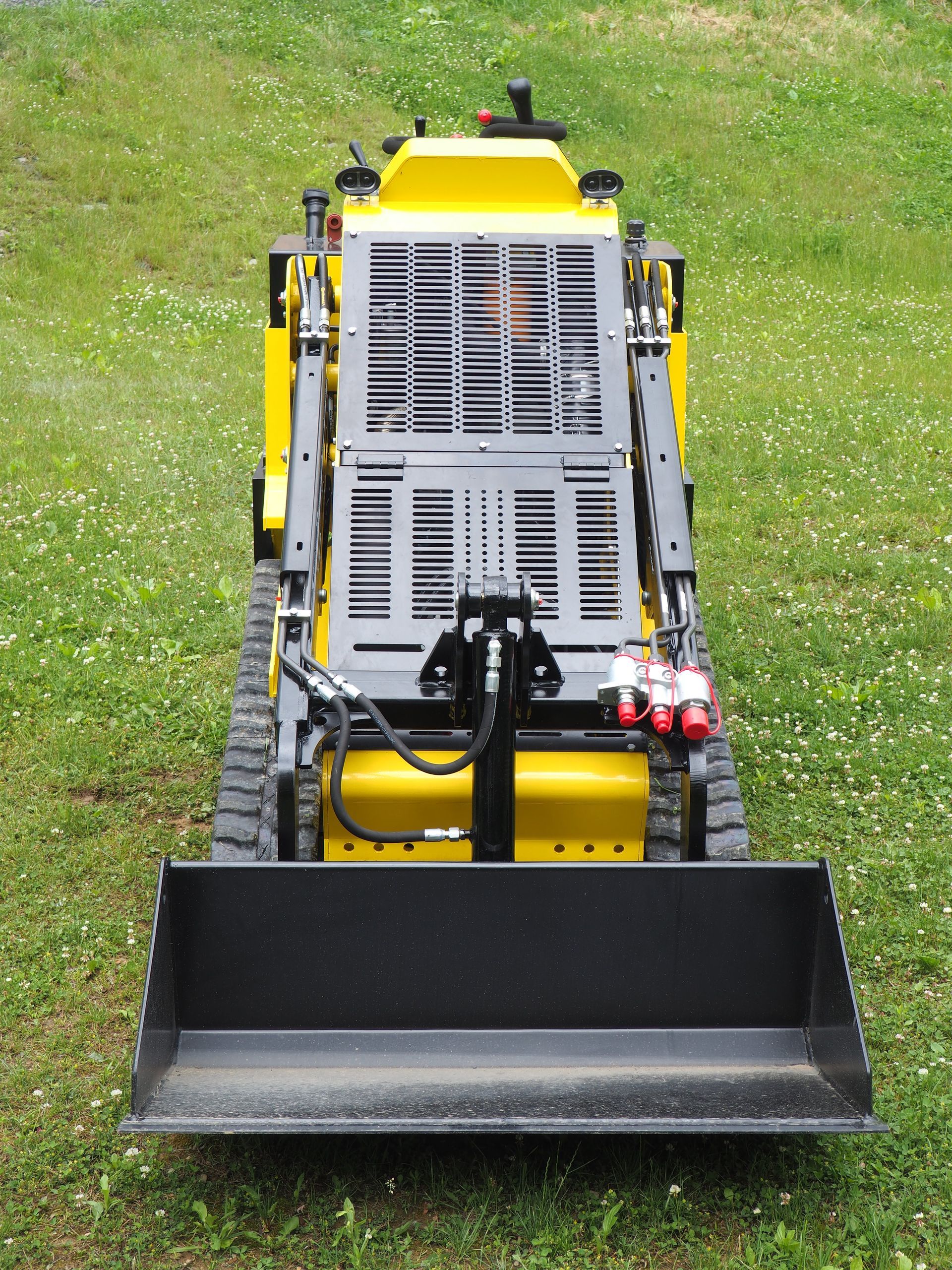Yellow compact track loader with black bucket on a grassy lawn.