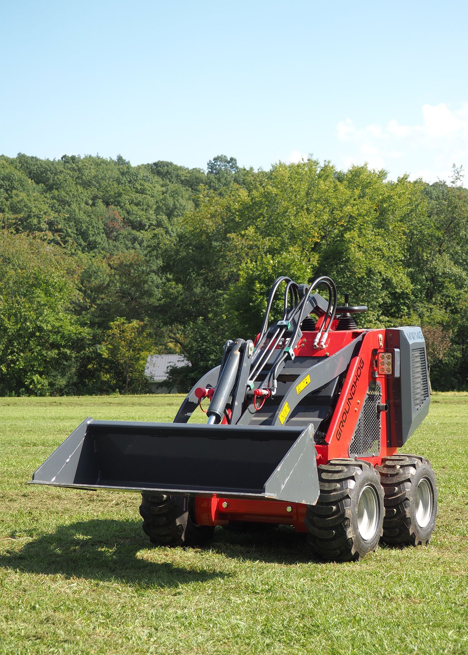 Red mini skid steer loader with a bucket in a grassy field.