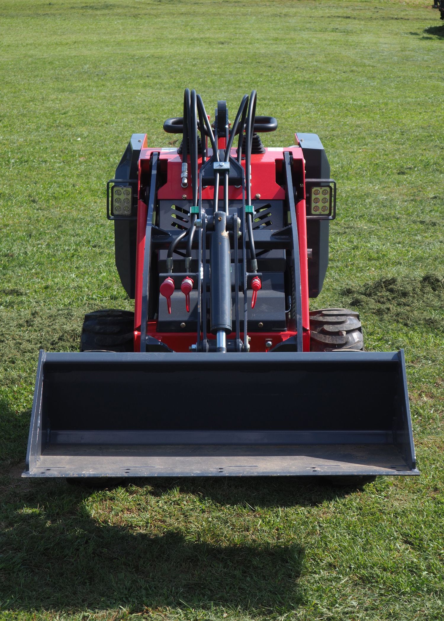 Red mini-skid steer loader with bucket on a grassy field.