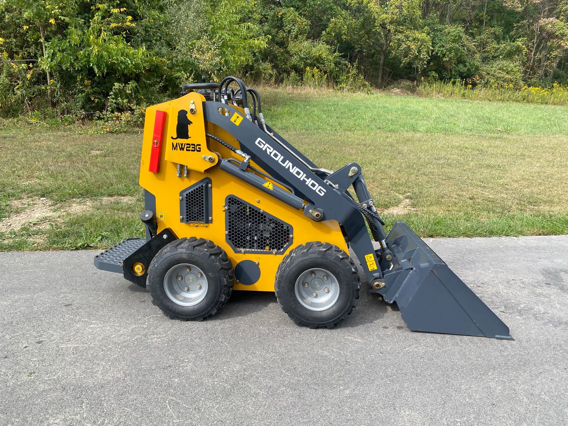 Yellow and black mini skid steer loader with a bucket on an asphalt surface.