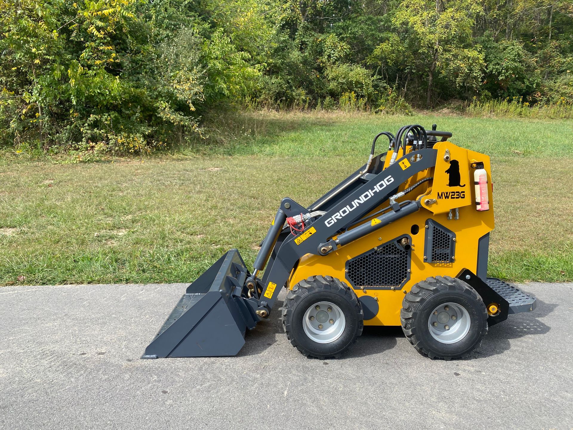 Yellow Carolina Hog mini skid steer loader with bucket parked on pavement.