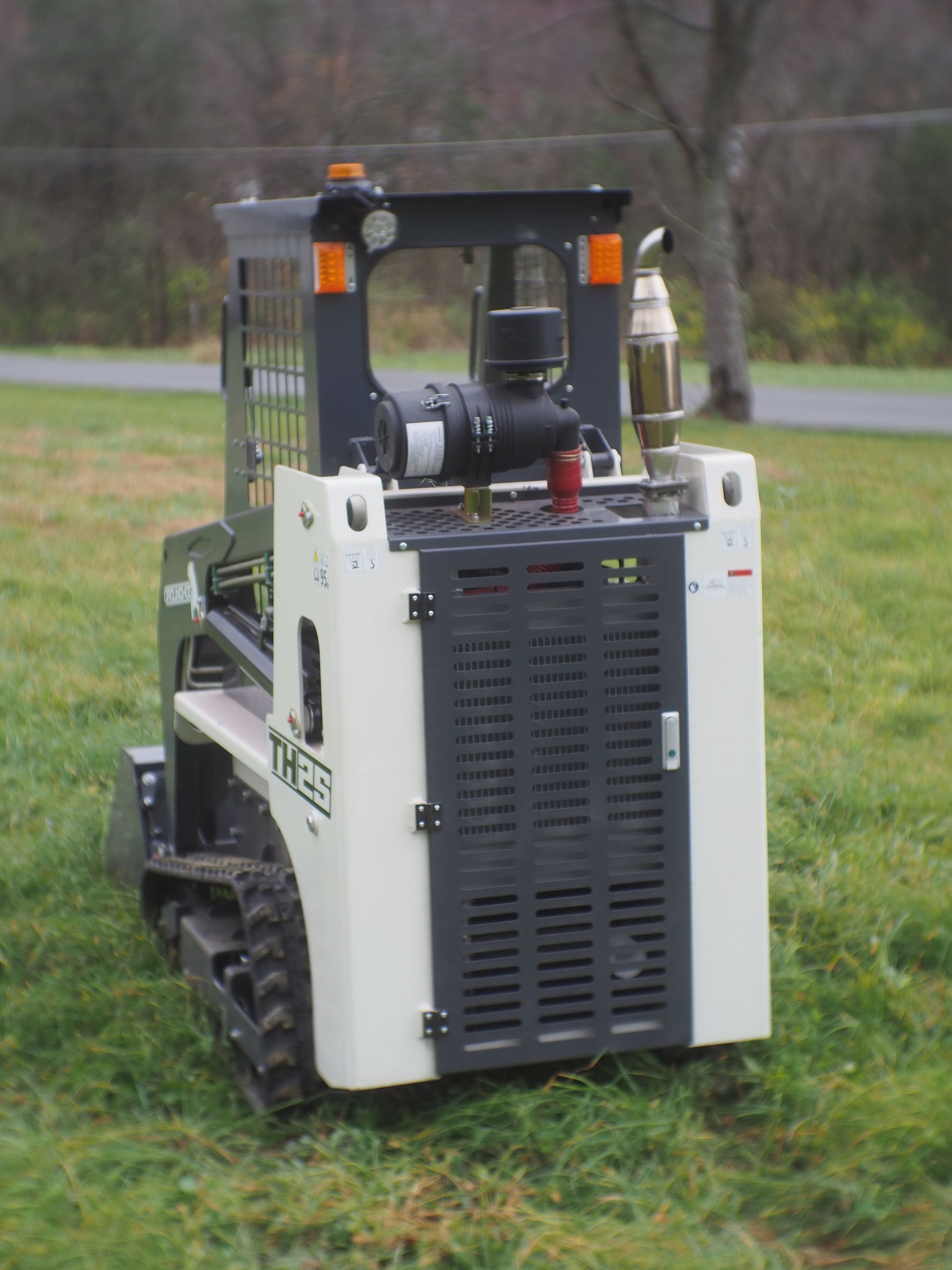 White and gray tracked vehicle on grass, with a black frame and various attachments.