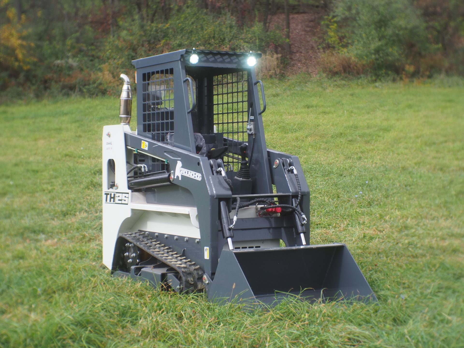 Tracked skid steer loader with bucket on a grassy field.