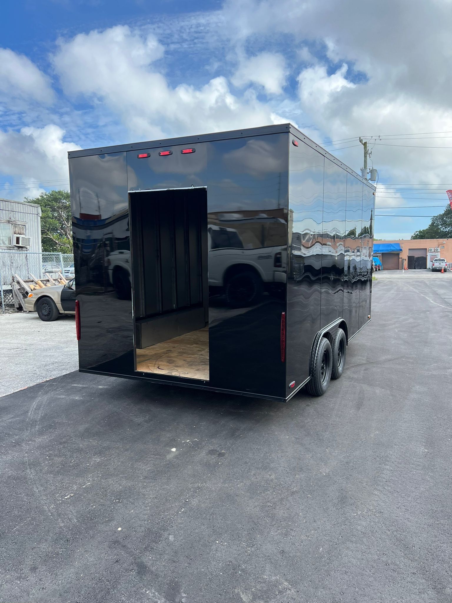 Black enclosed cargo trailer with open rear door, parked on a gravel lot under a cloudy sky.