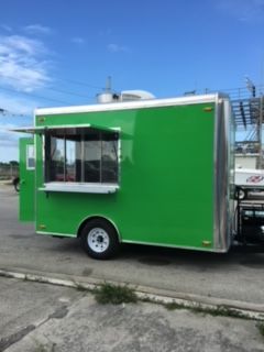 Green food trailer with serving window parked outdoors on pavement