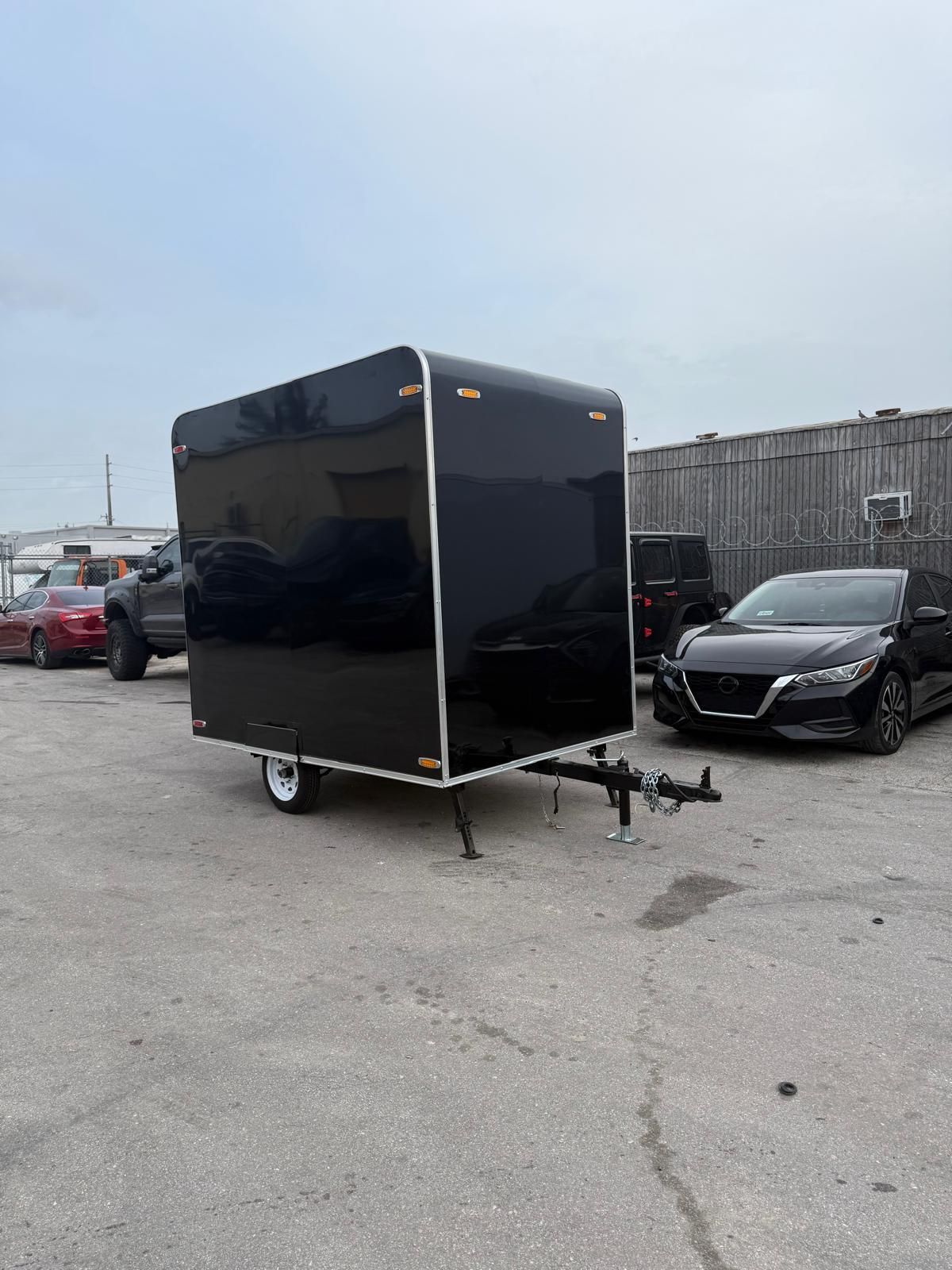 Black enclosed cargo trailer parked in a lot beside a black car and other vehicles