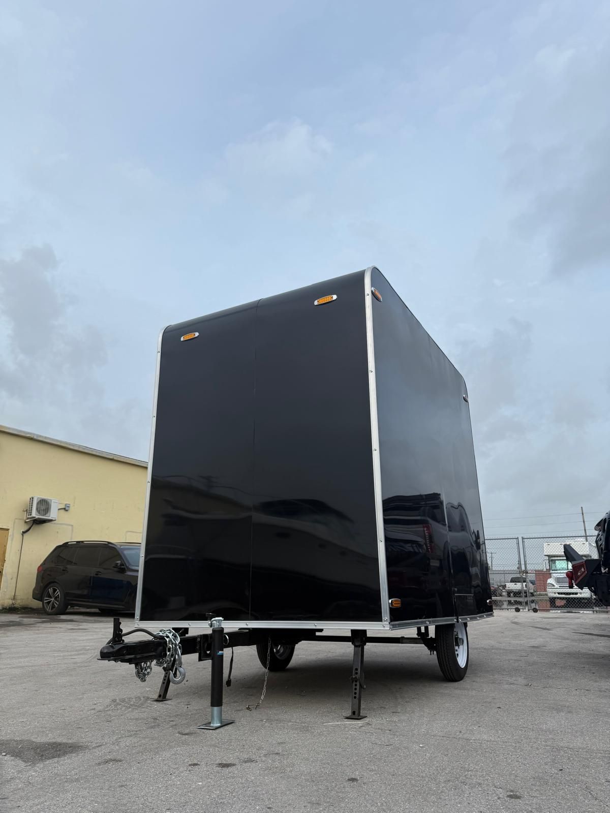 Black enclosed utility trailer on a parking lot with a cloudy sky overhead