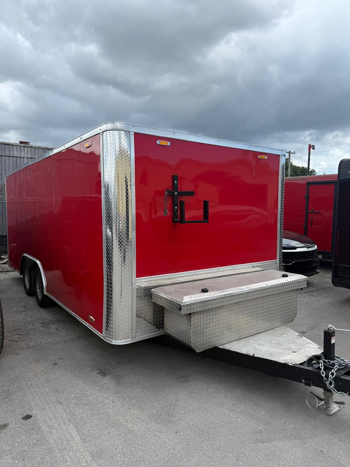Red enclosed utility trailer with diamond-plate trim parked in a lot under cloudy skies