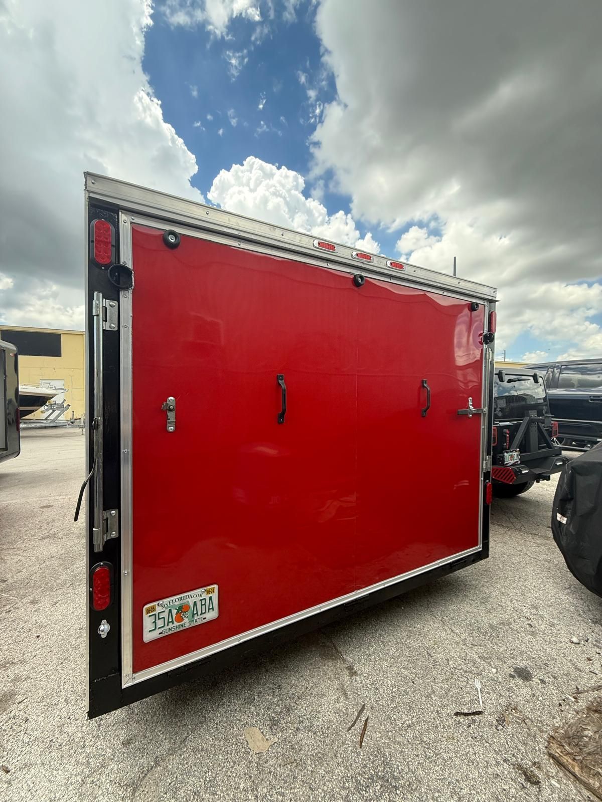 Red enclosed utility trailer with black trim parked on a gravel lot under a cloudy sky