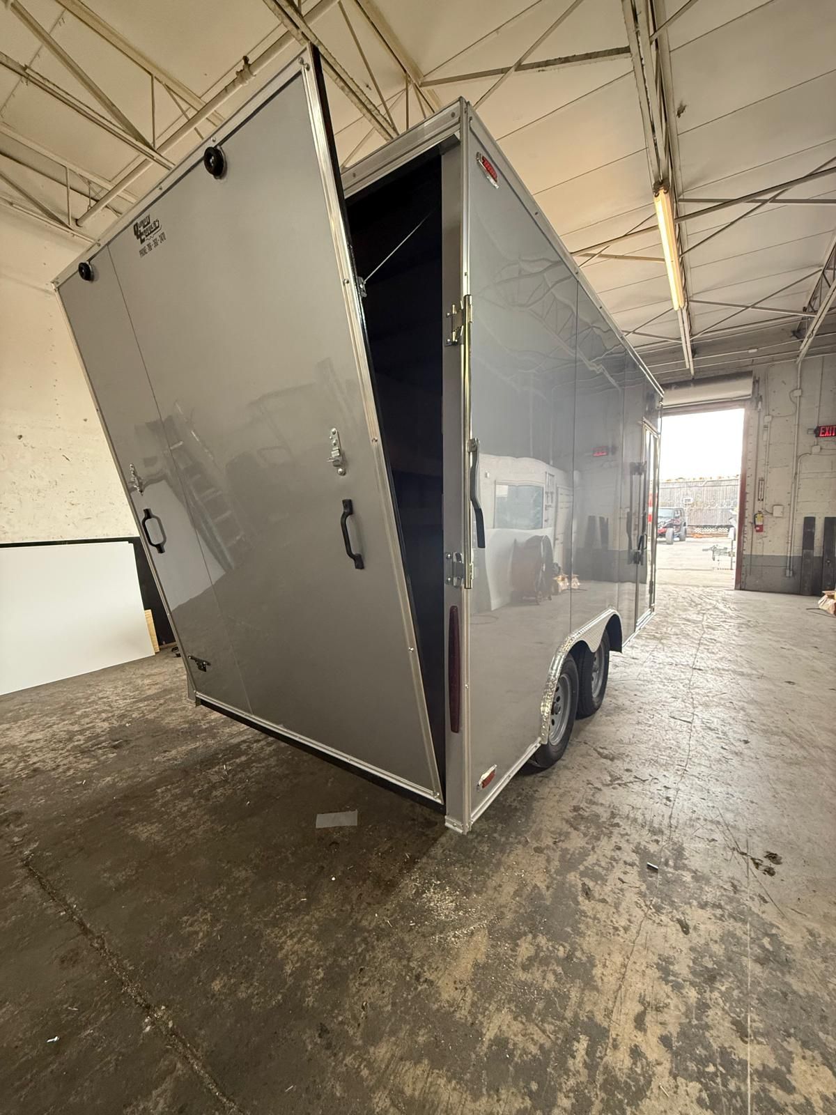Silver enclosed cargo trailer with rear door open inside a warehouse